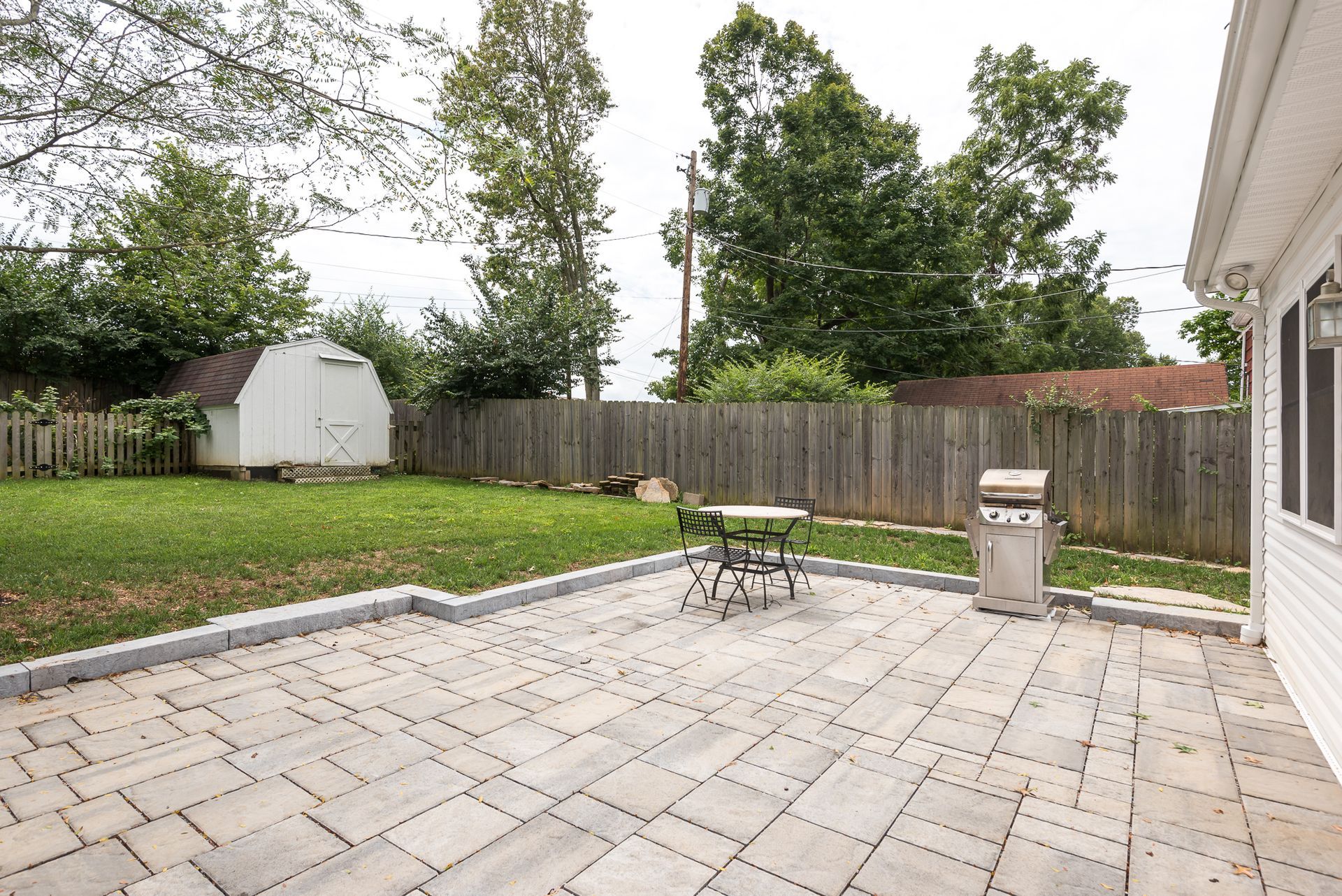A patio with a table and chairs and a grill in the backyard of a house.