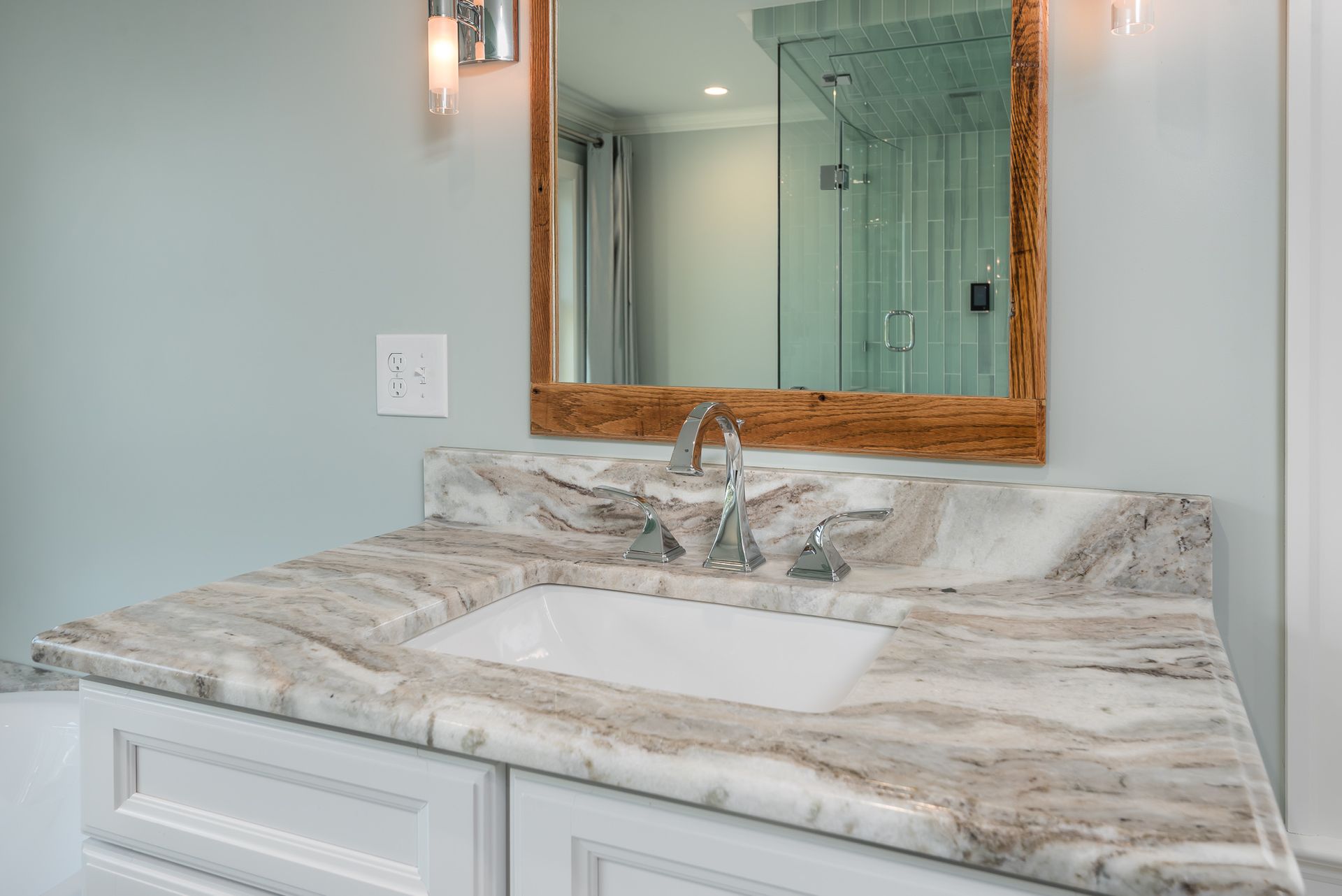 A bathroom with a sink , mirror and marble counter top.