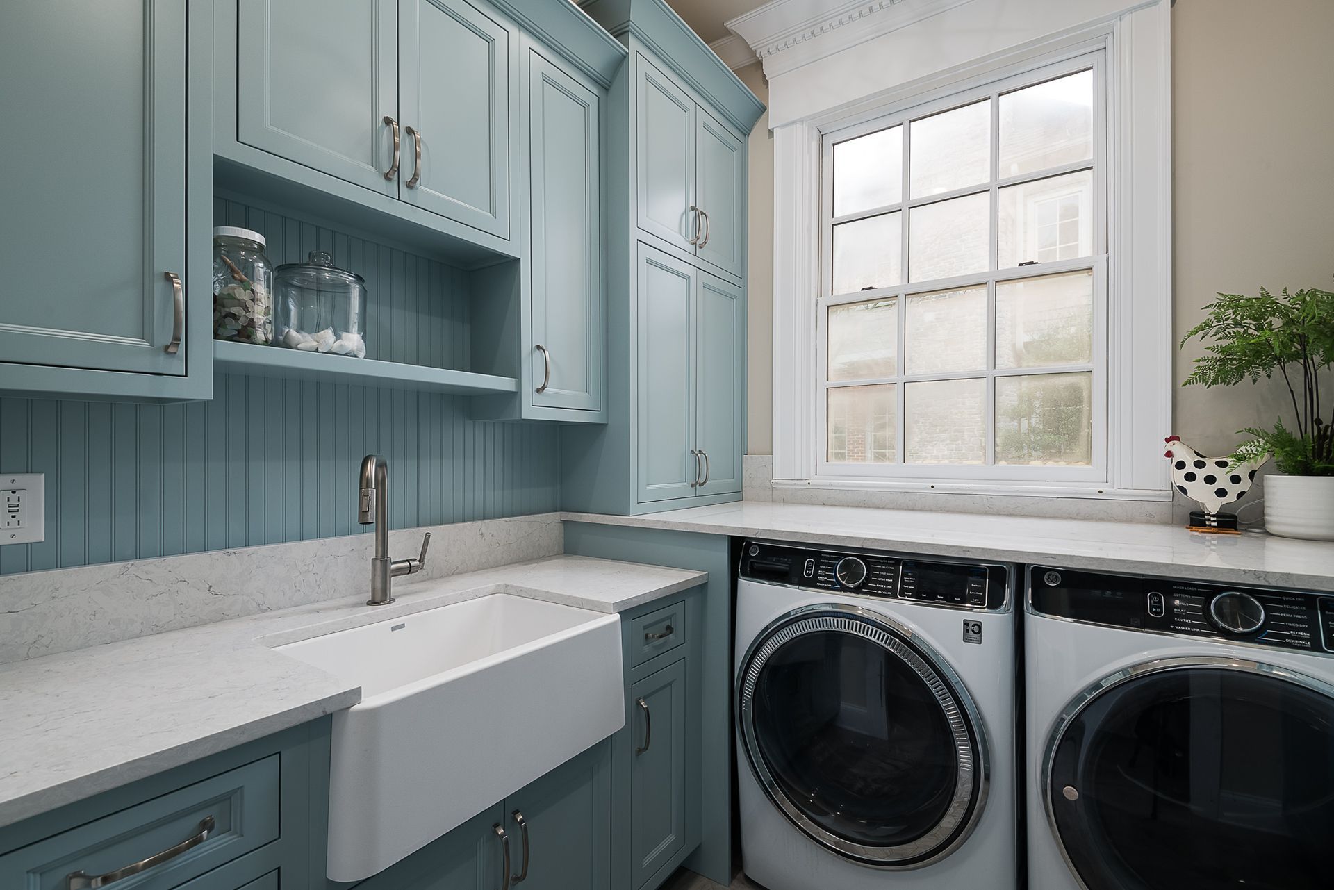 A laundry room with blue cabinets , a washer and dryer , a sink , and a window.