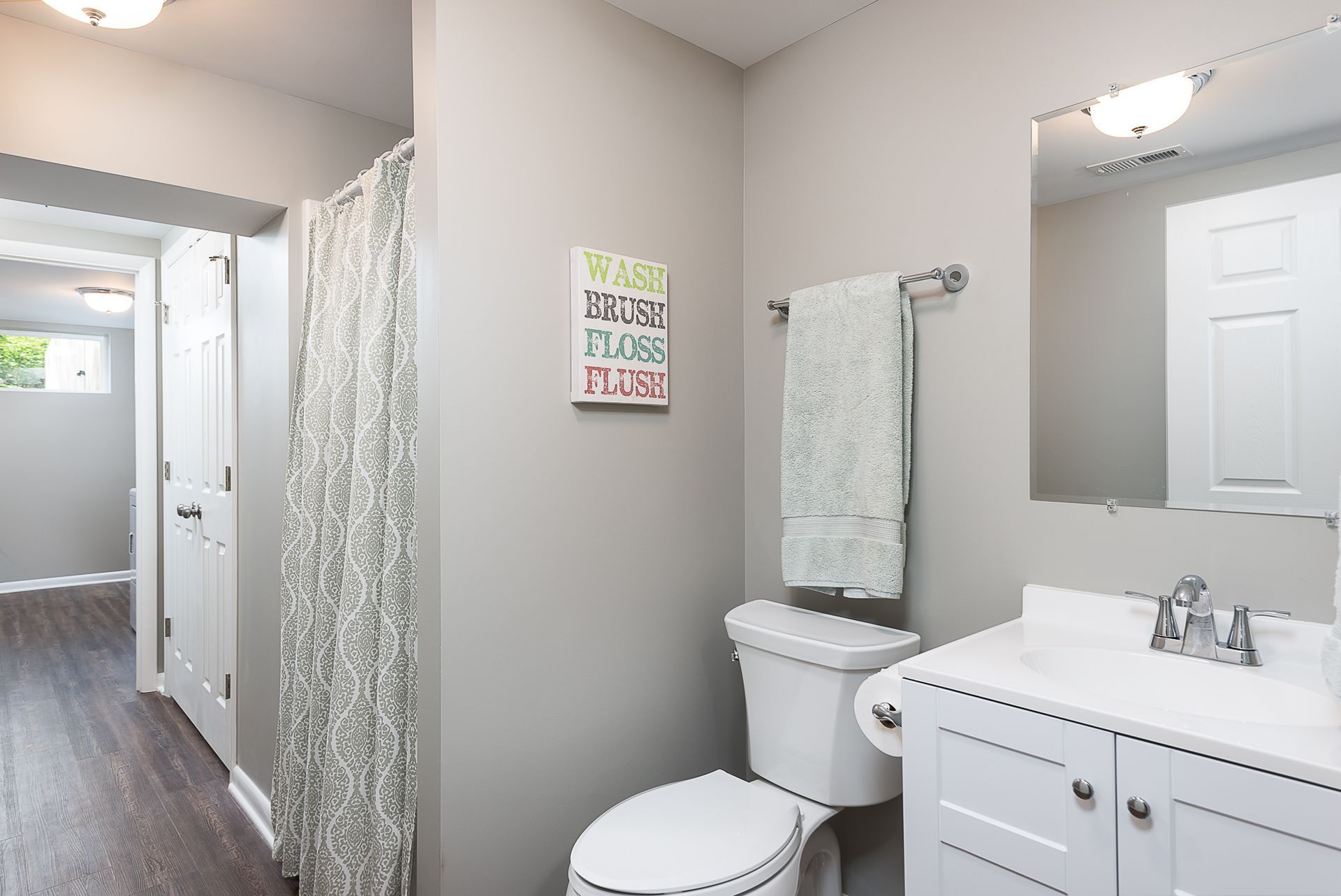 A bathroom with a toilet , sink , mirror and shower curtain.