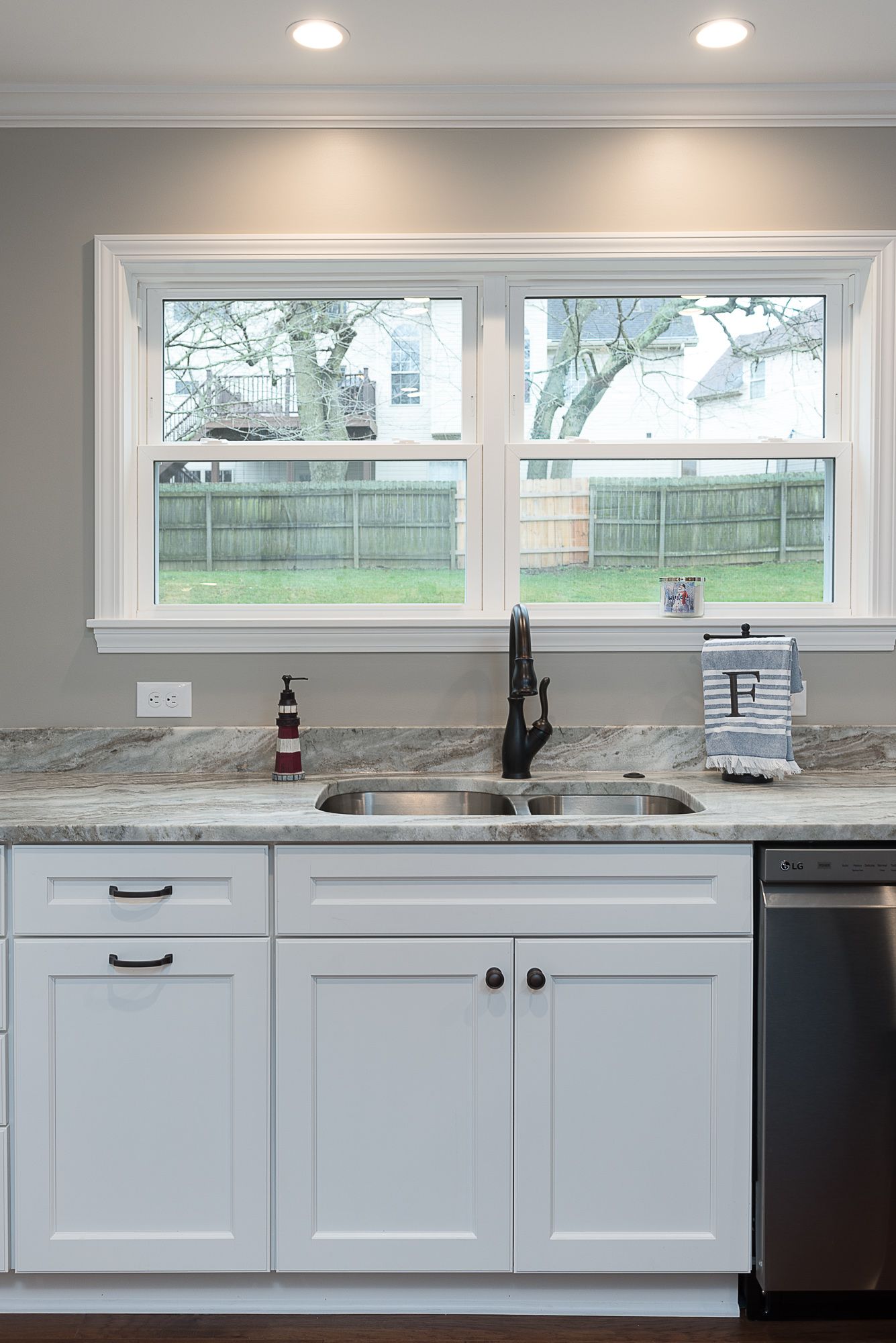 A kitchen with white cabinets , a sink , and a window.