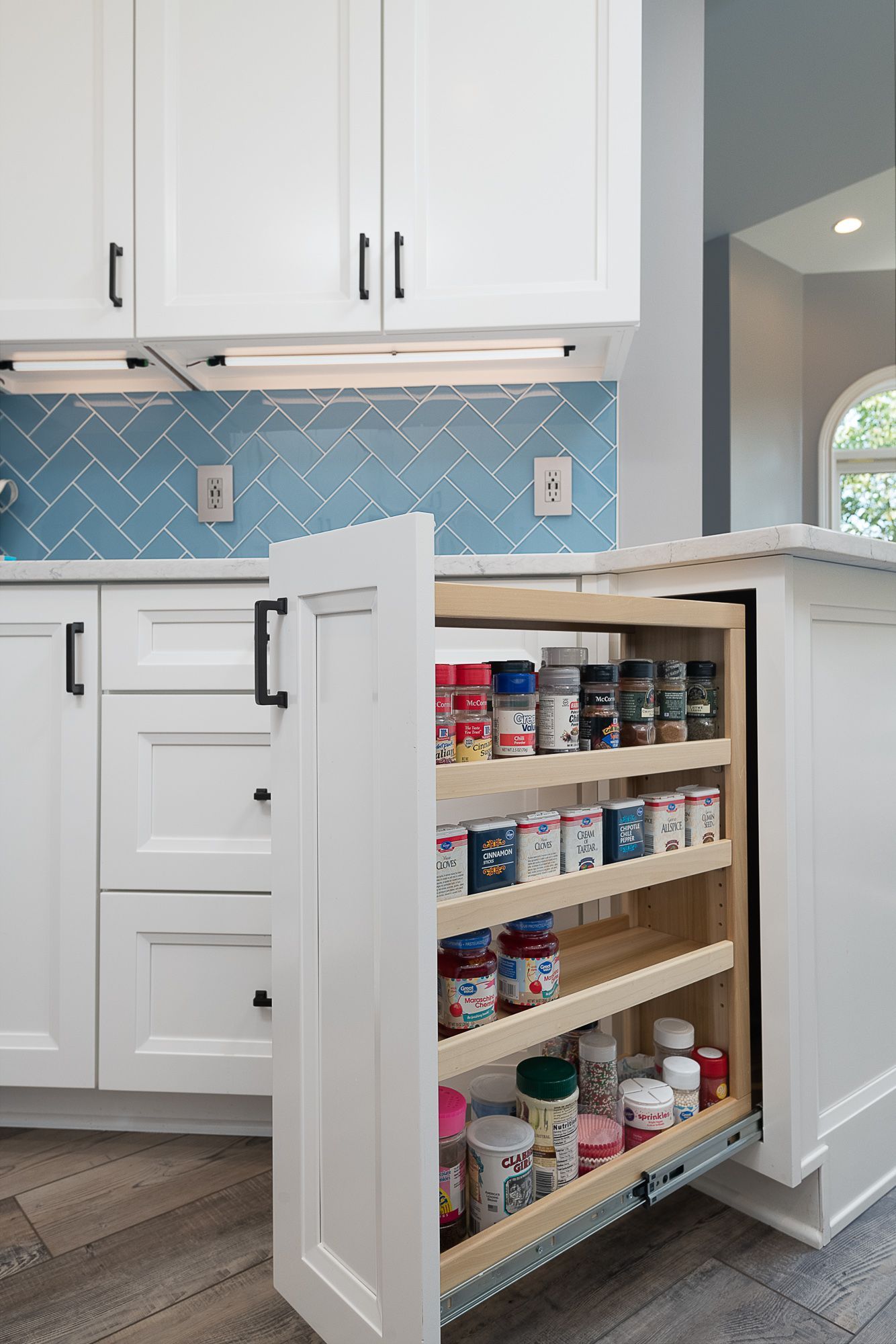 A kitchen with white cabinets and a pull out spice rack.