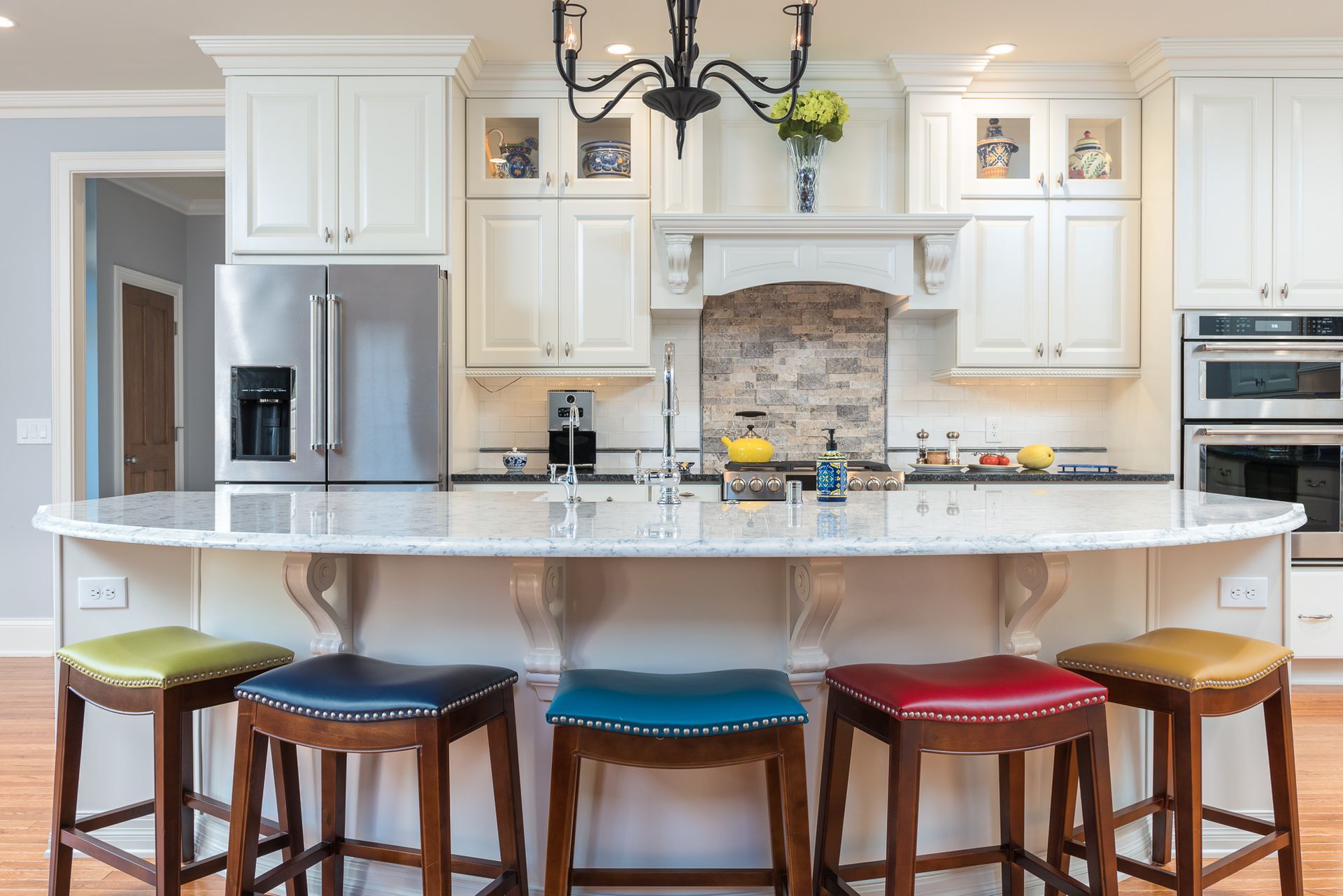 A kitchen with white cabinets , stools , a refrigerator and a chandelier.