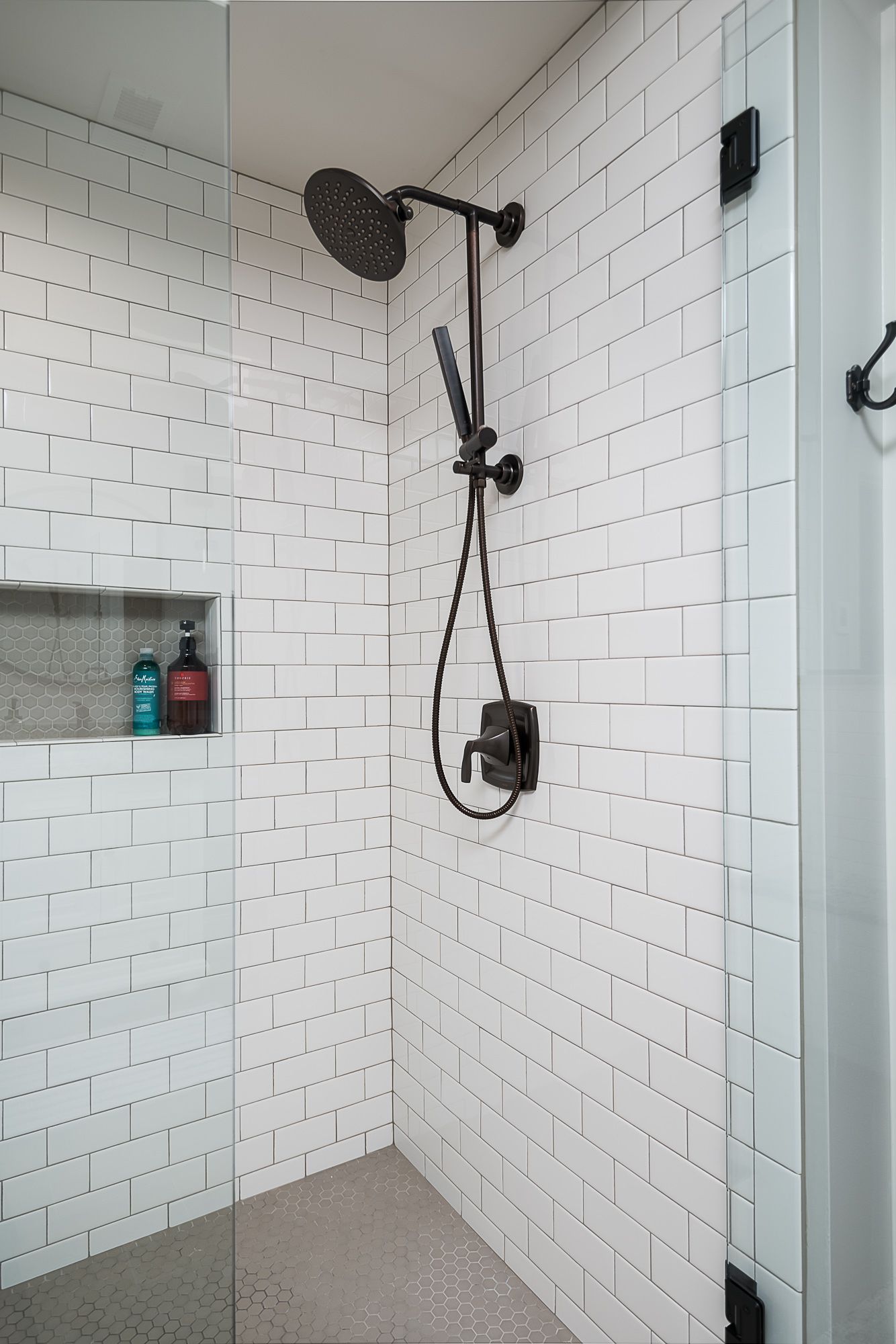 A shower with white tiles and a black shower head