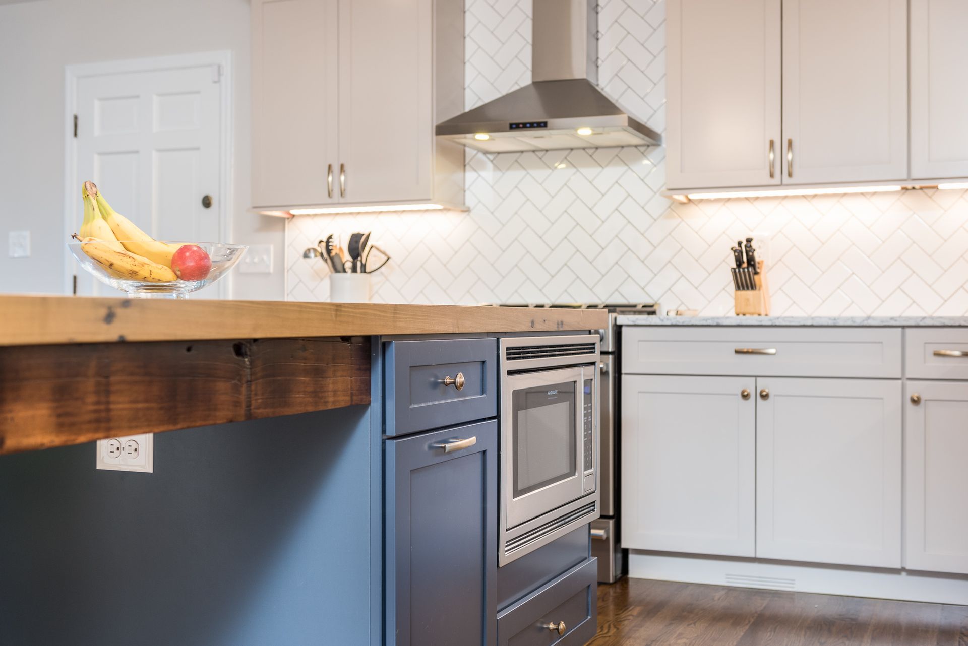 A kitchen with stainless steel appliances , white cabinets , and a wooden counter top.