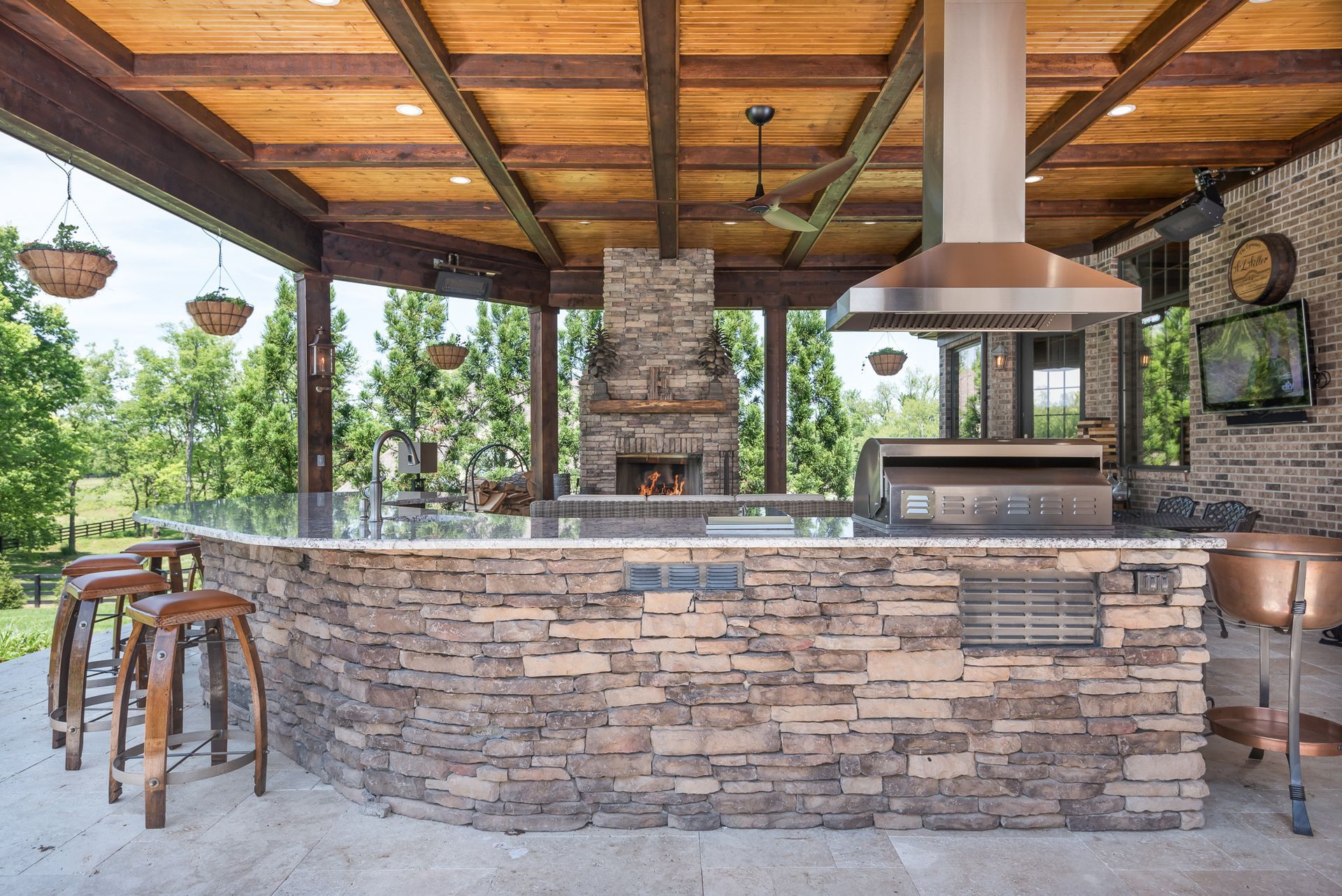 A large outdoor kitchen with a wooden ceiling and stools.
