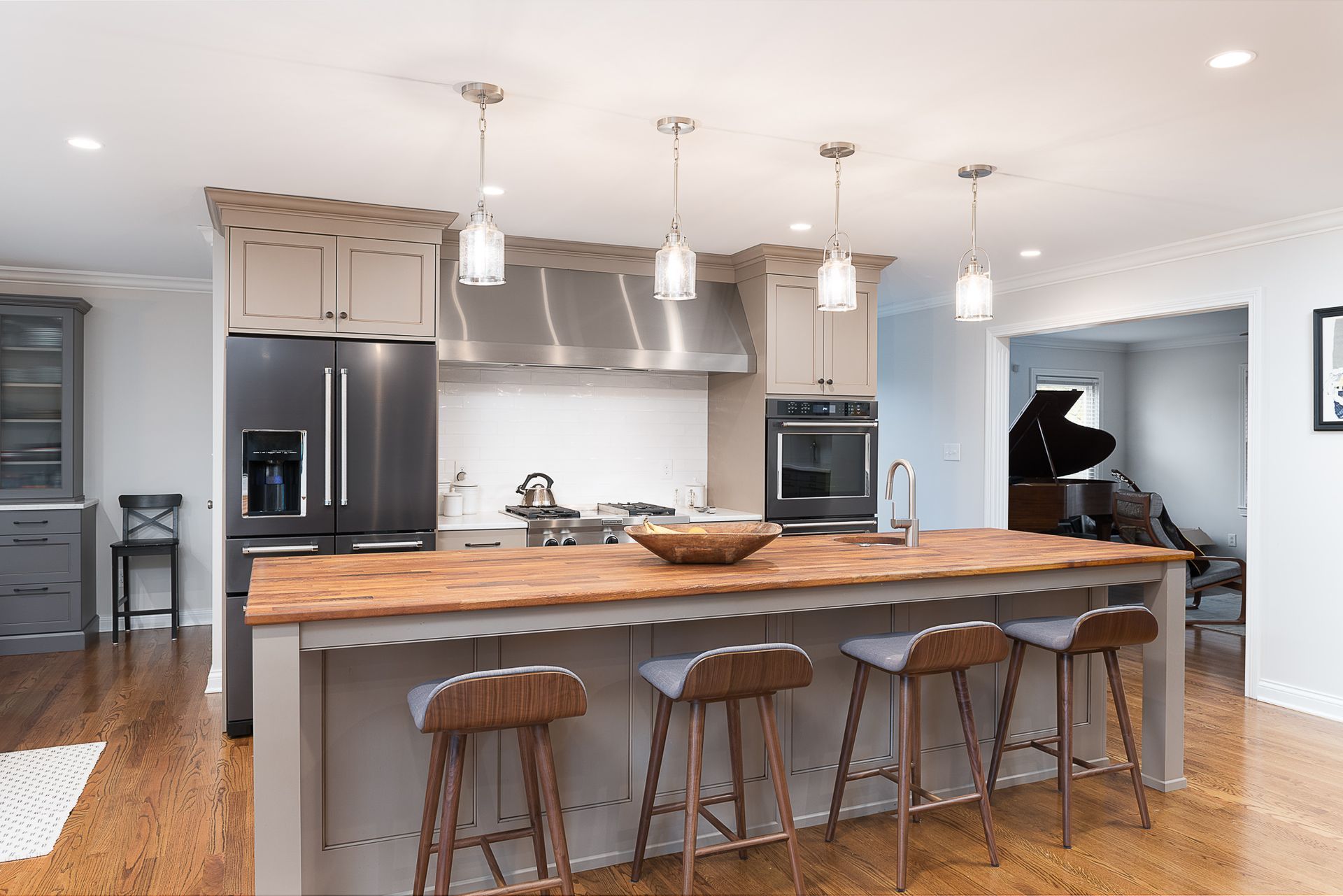 A kitchen with a large island and stools and a piano in the background.