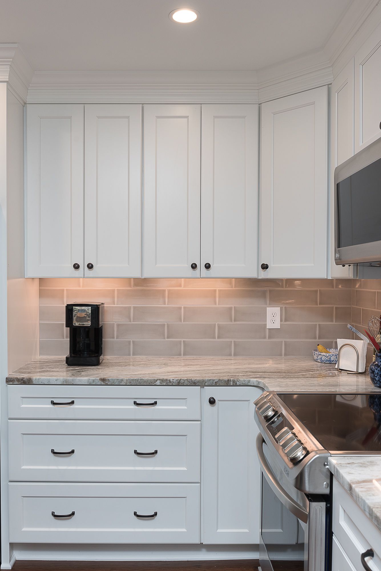 A kitchen with white cabinets , a stove , a microwave , and a coffee maker.