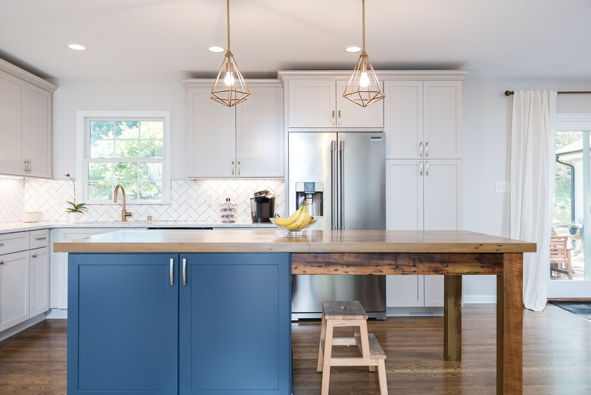 A kitchen with blue cabinets , white cabinets , stainless steel appliances and a wooden table.