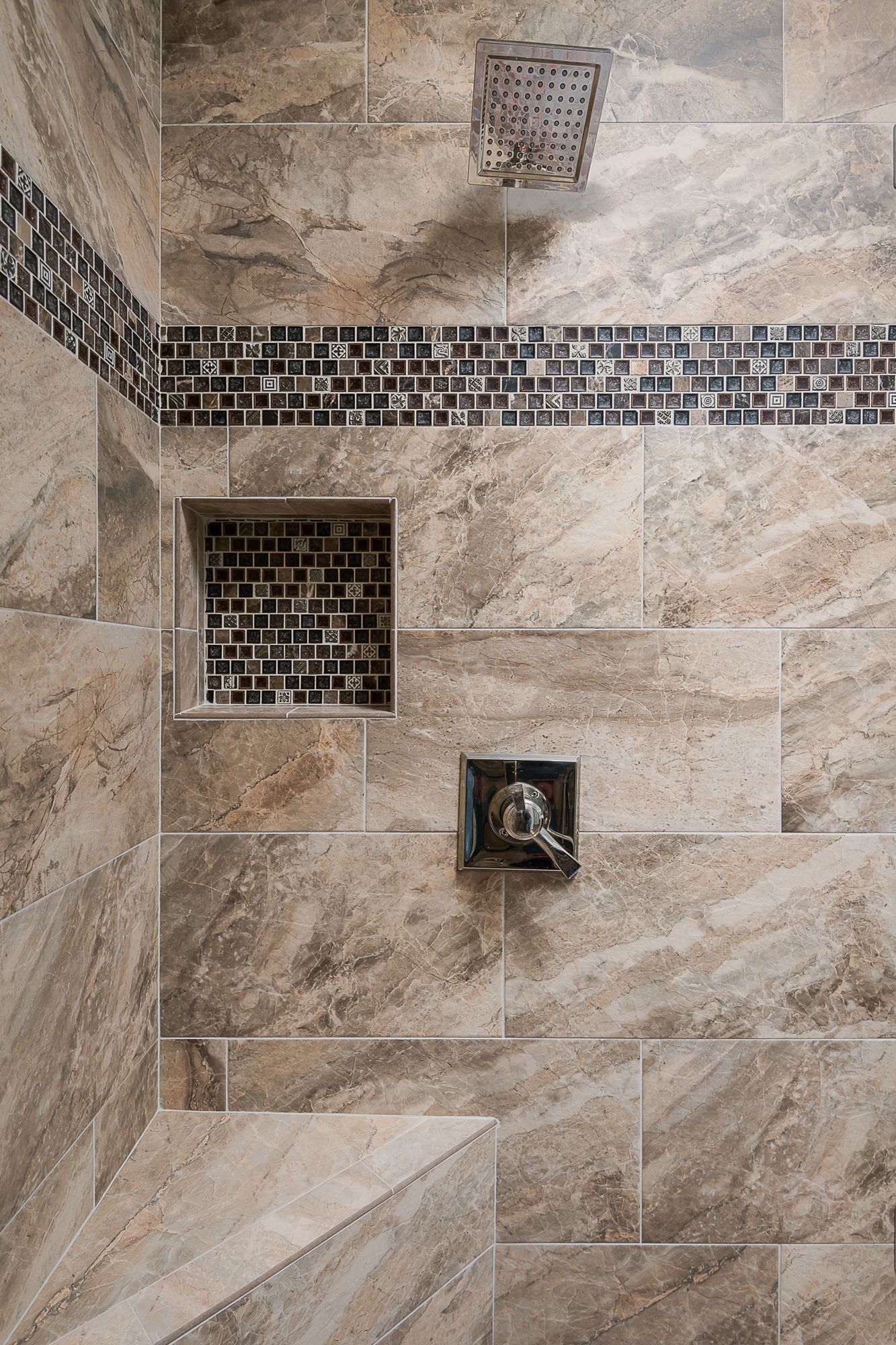 A close up of a shower with tile walls and a shower head.