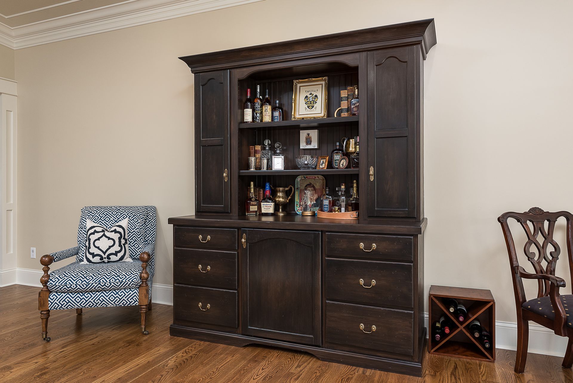 A living room with a hutch filled with bottles and a chair