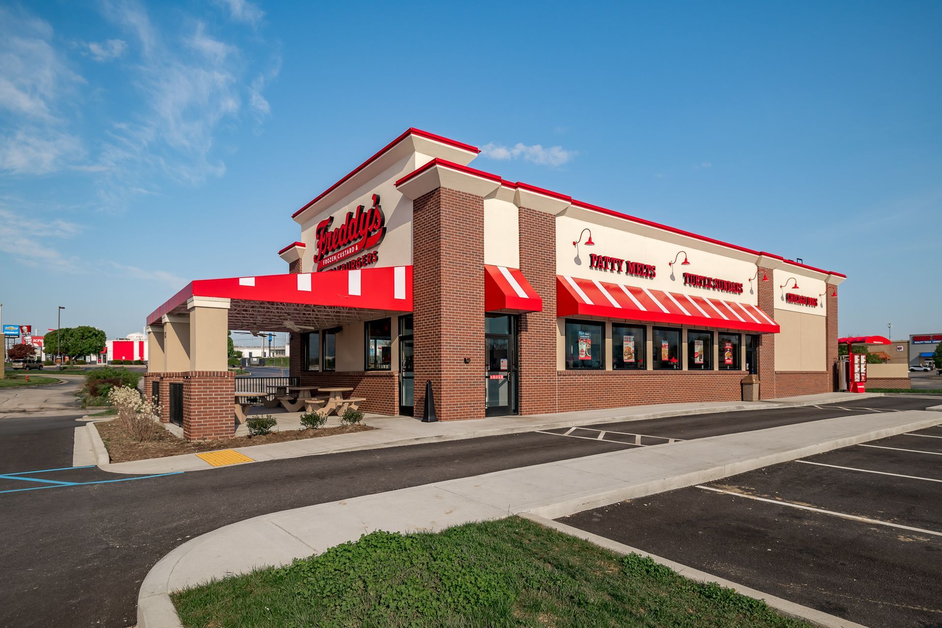 A fast food restaurant with a red awning and a parking lot in front of it.