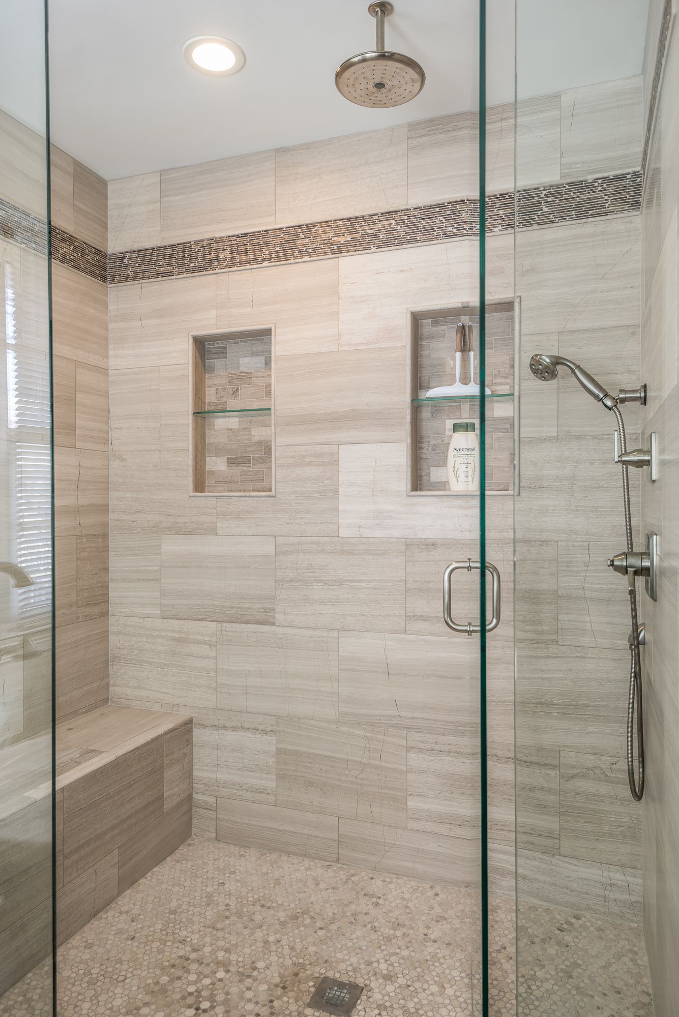 A walk in shower with a glass door and a bench.