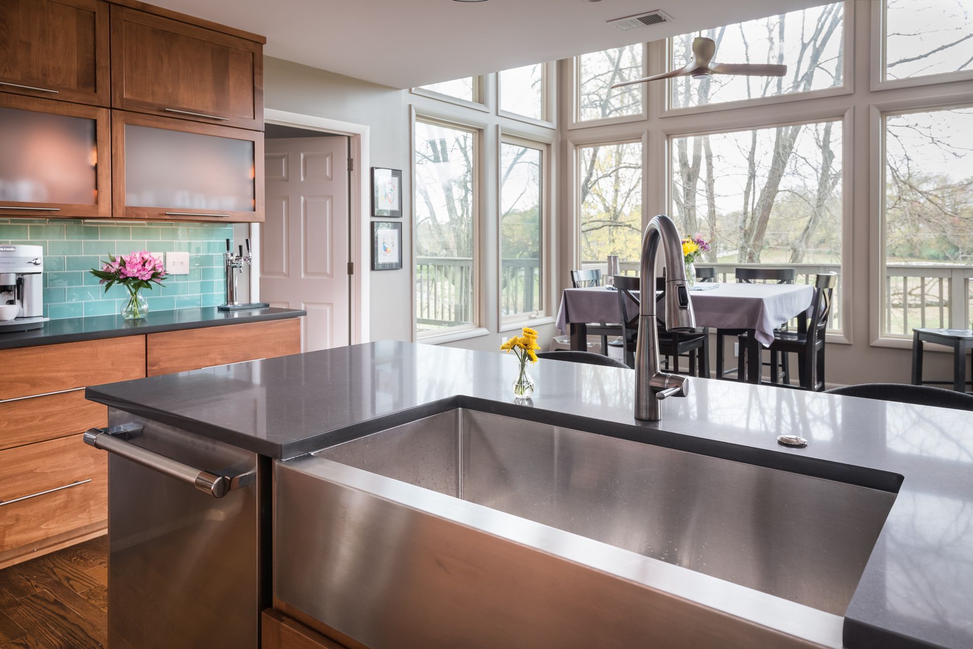 A kitchen with a large stainless steel sink and a dining room in the background.