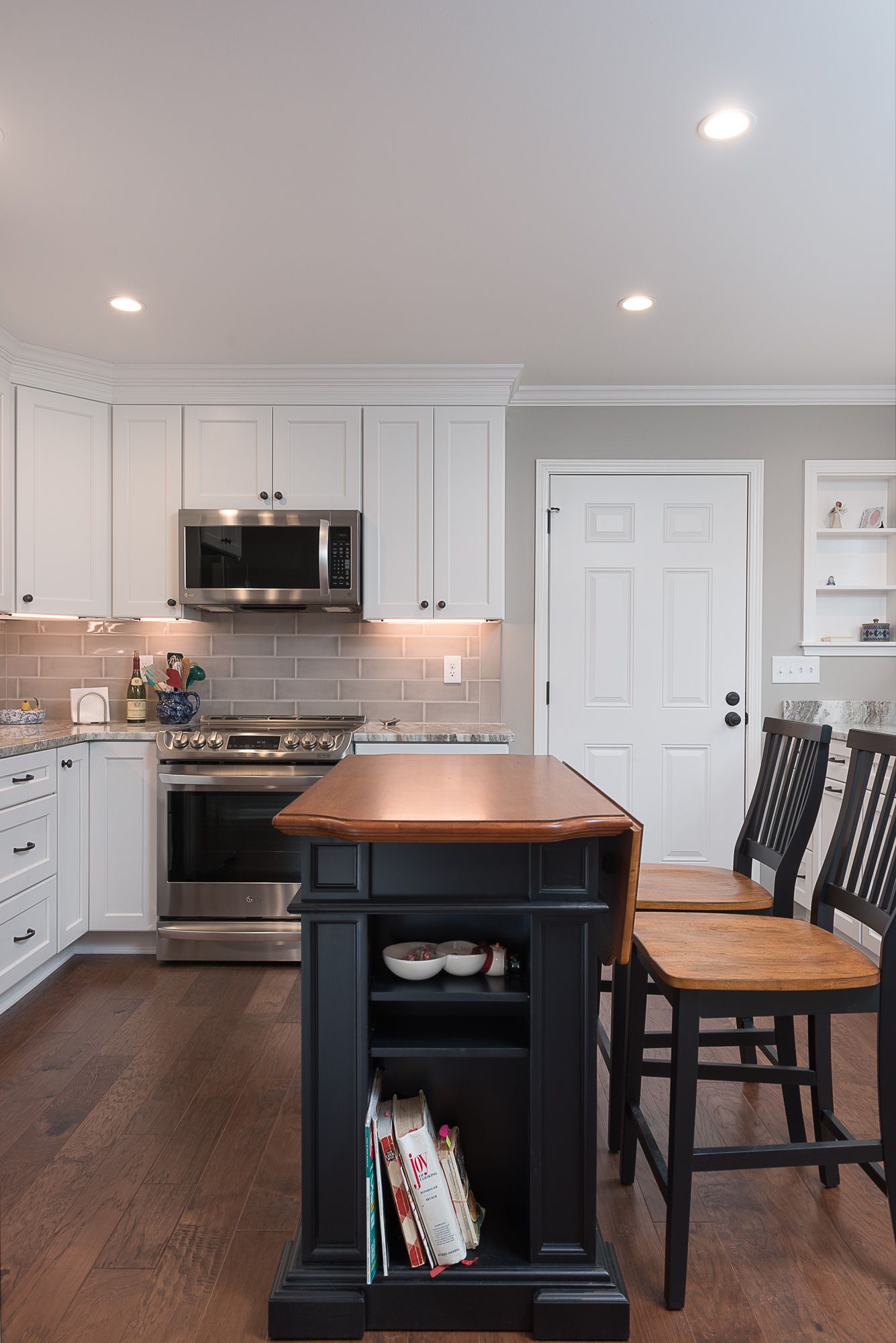 A kitchen with white cabinets , stainless steel appliances , a black island , and wooden chairs.