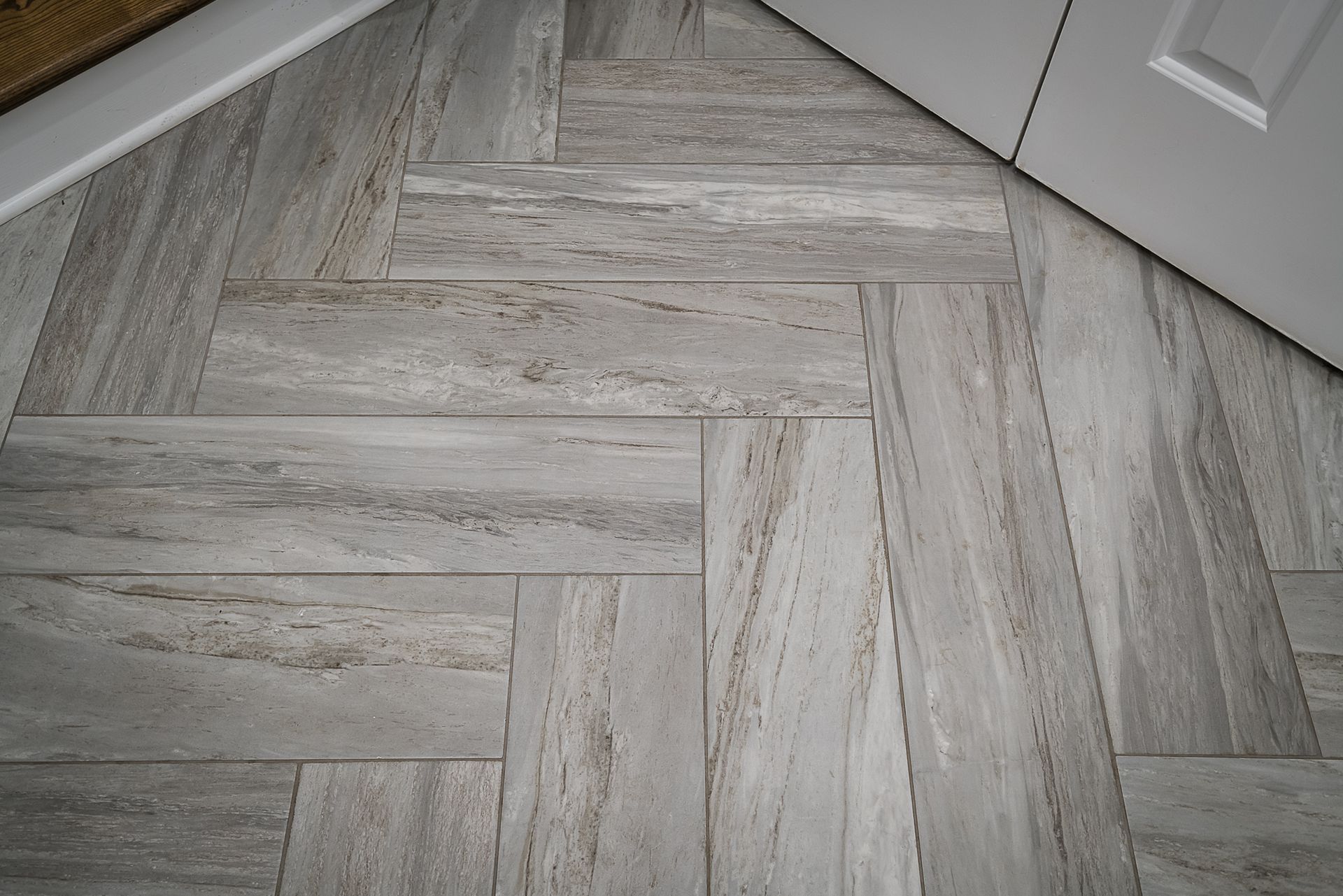 A close up of a herringbone tile floor next to a door.