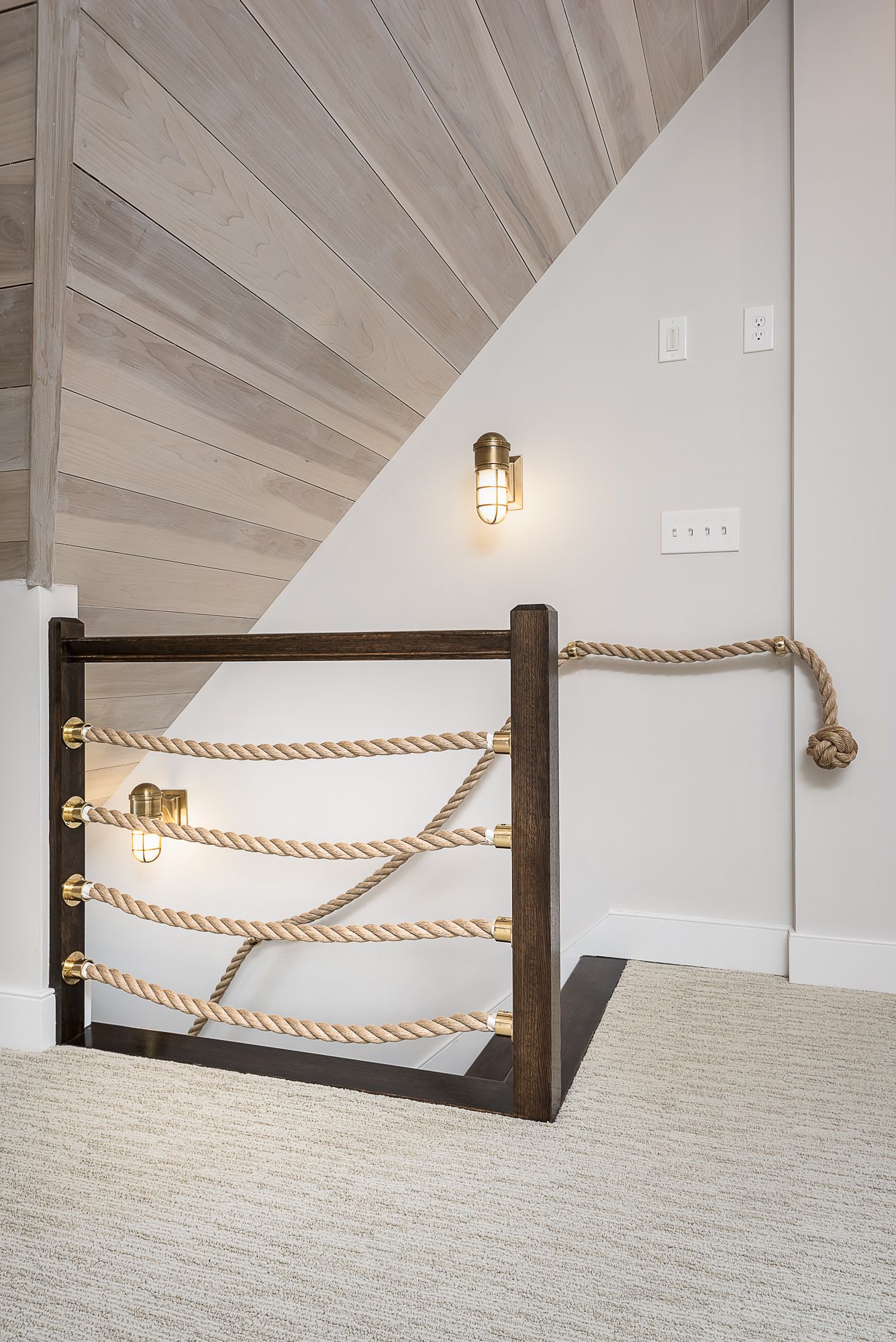 A wooden staircase with a rope railing and a light on the wall.