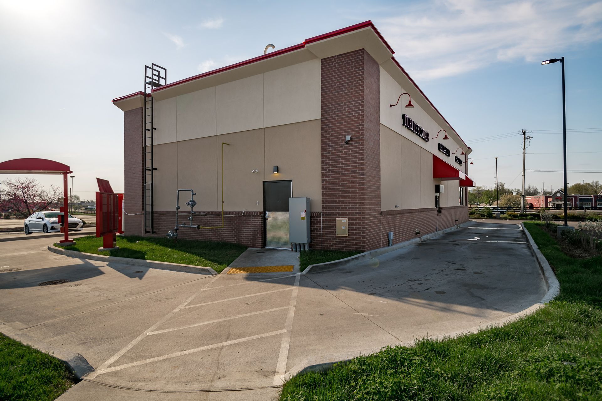 A large white building with a red awning and a parking lot in front of it.