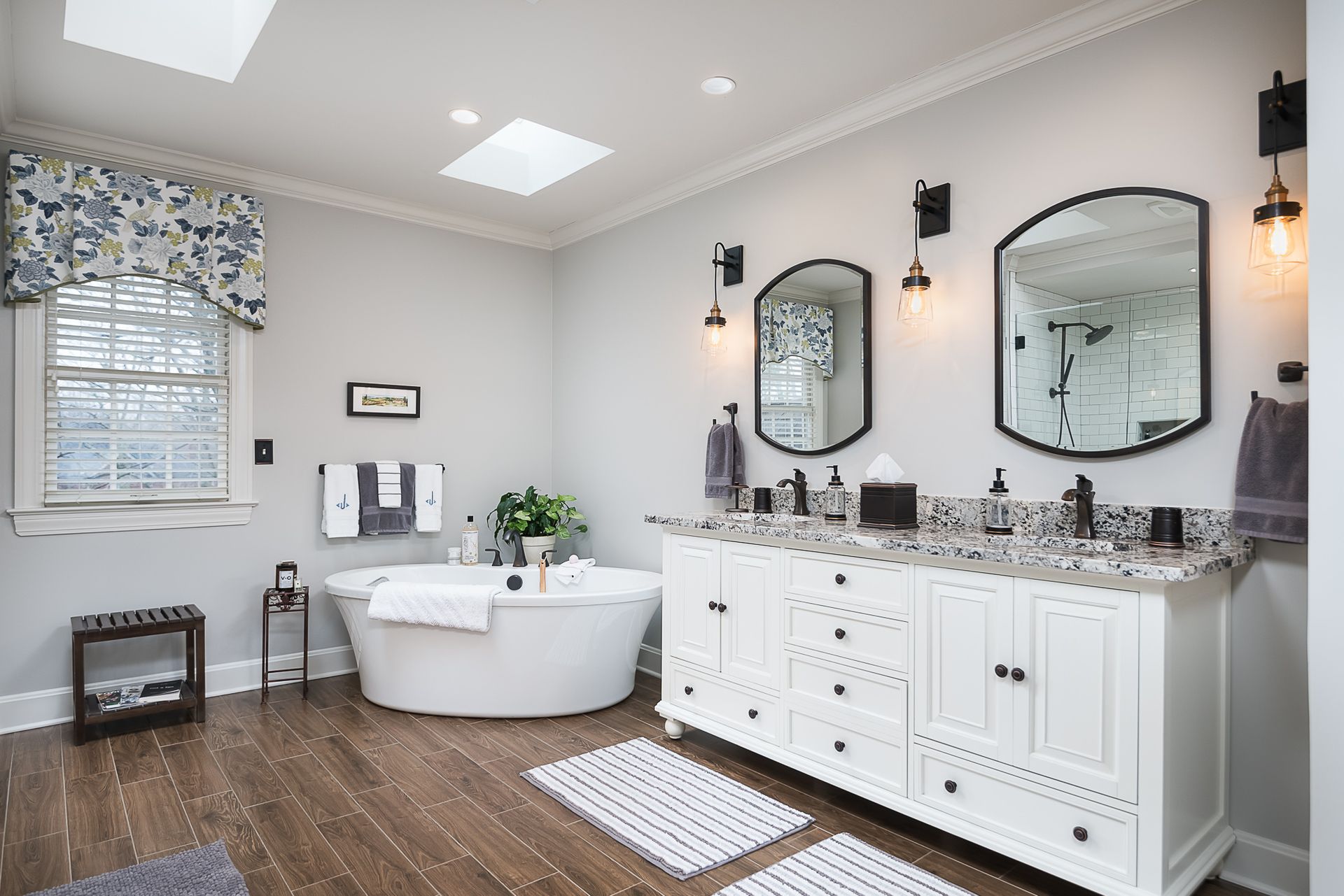 A bathroom with a tub , sinks , mirrors and a skylight.