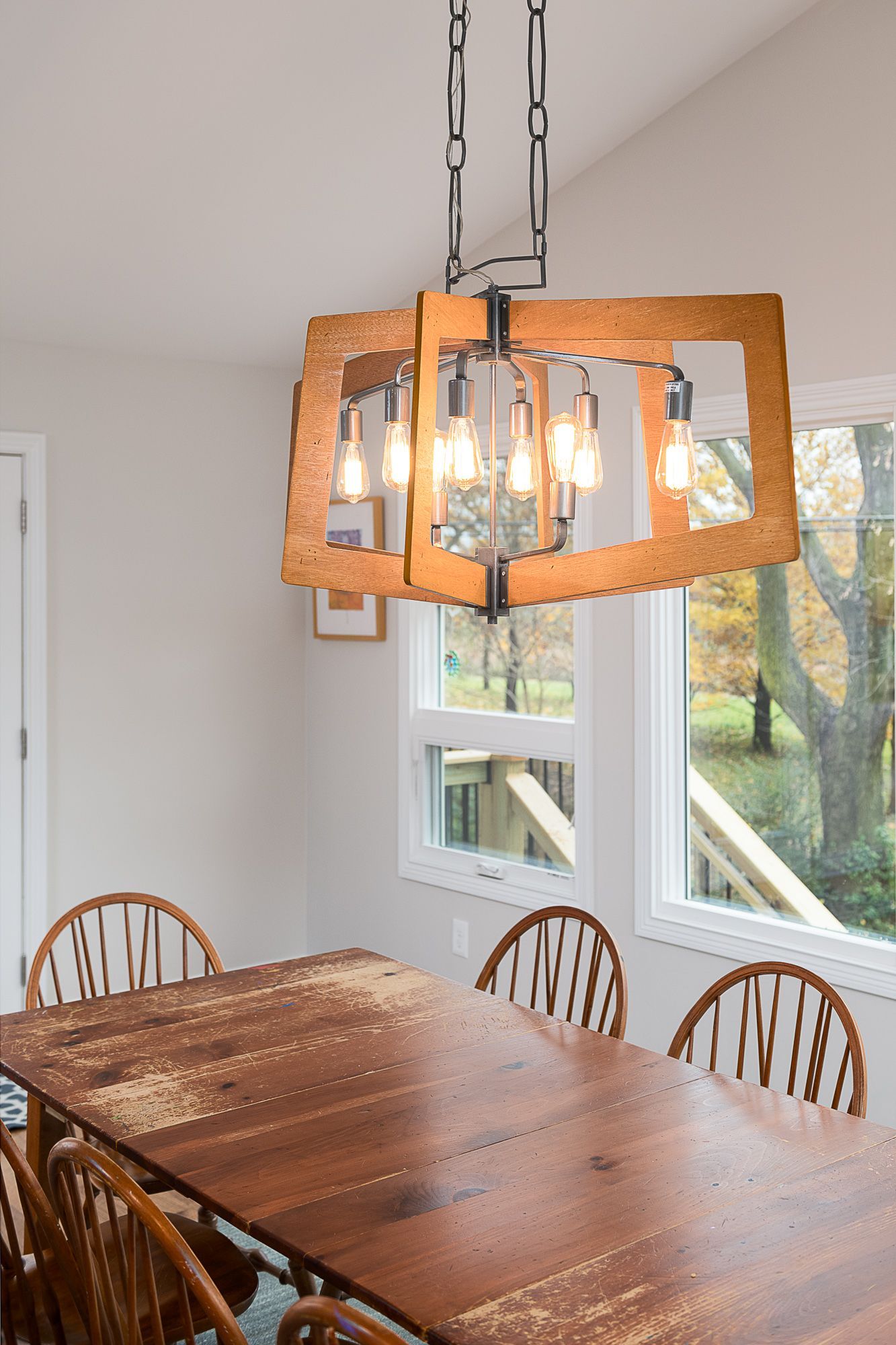 A dining room with a wooden table and chairs and a wooden chandelier hanging from the ceiling.