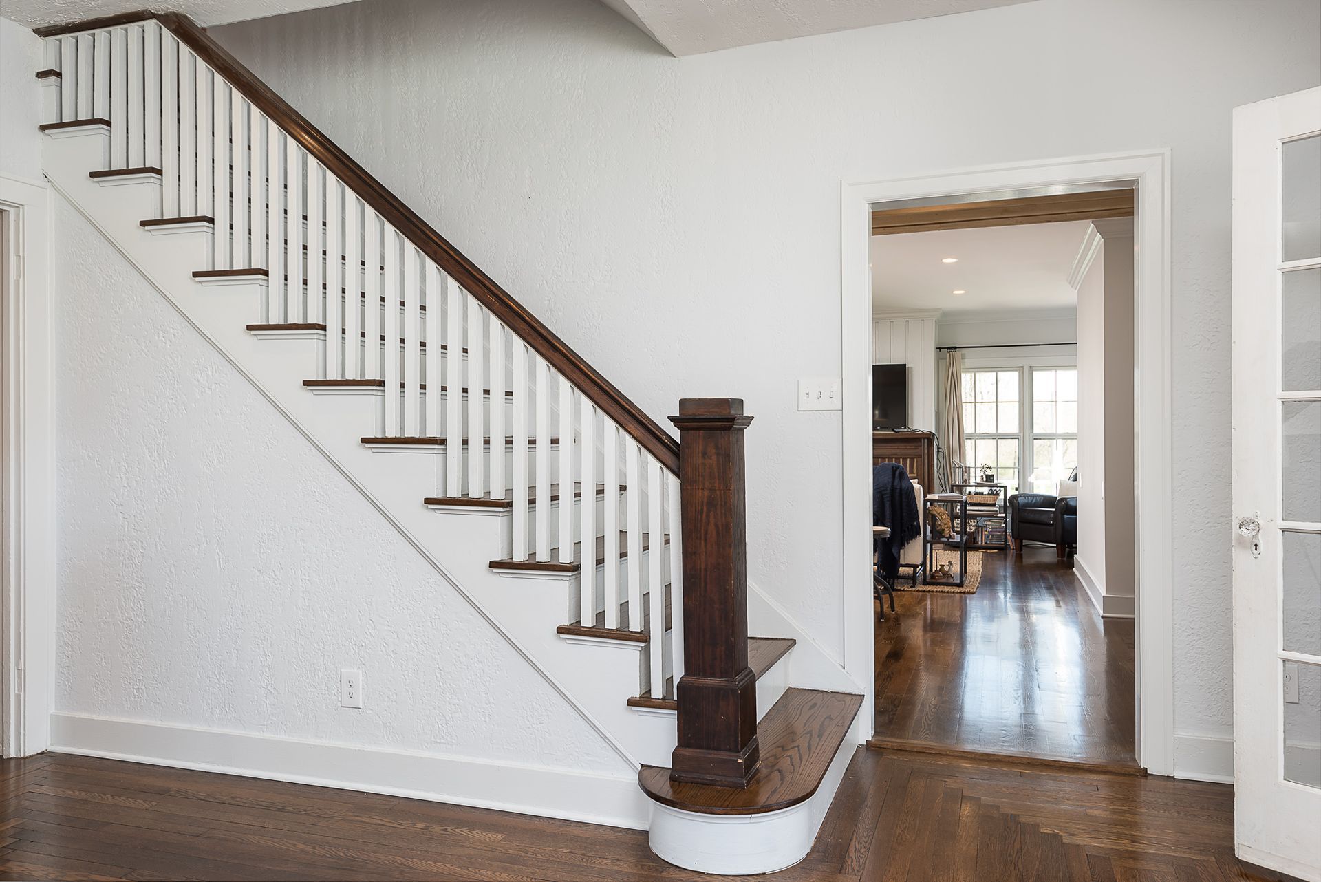 A wooden staircase with white railings is in a hallway leading to a living room.