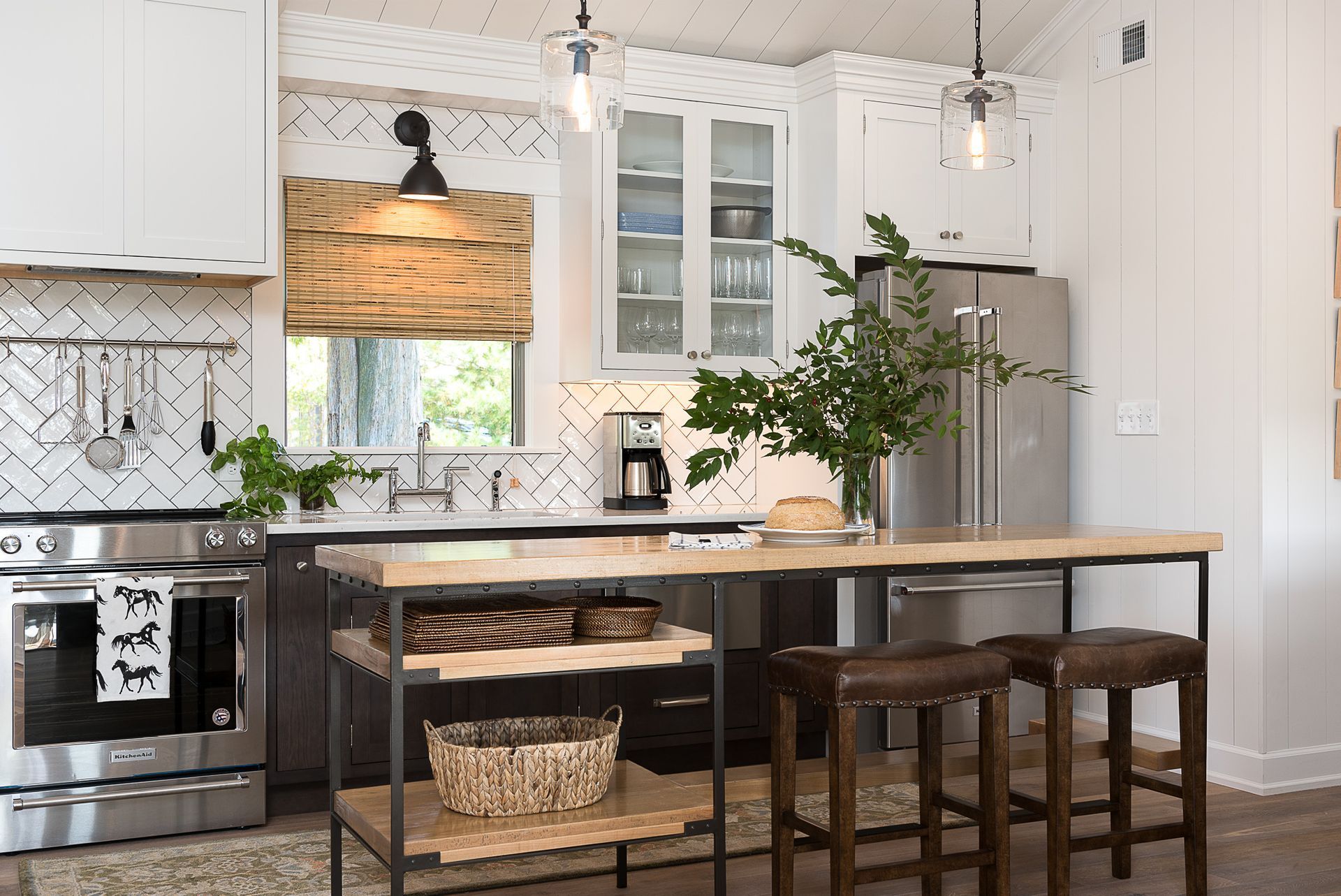 A kitchen with white cabinets , stainless steel appliances , a large island with a wooden table and stools.