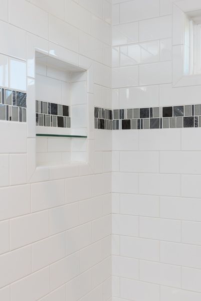 A bathroom with white tiles and a shelf in the shower.