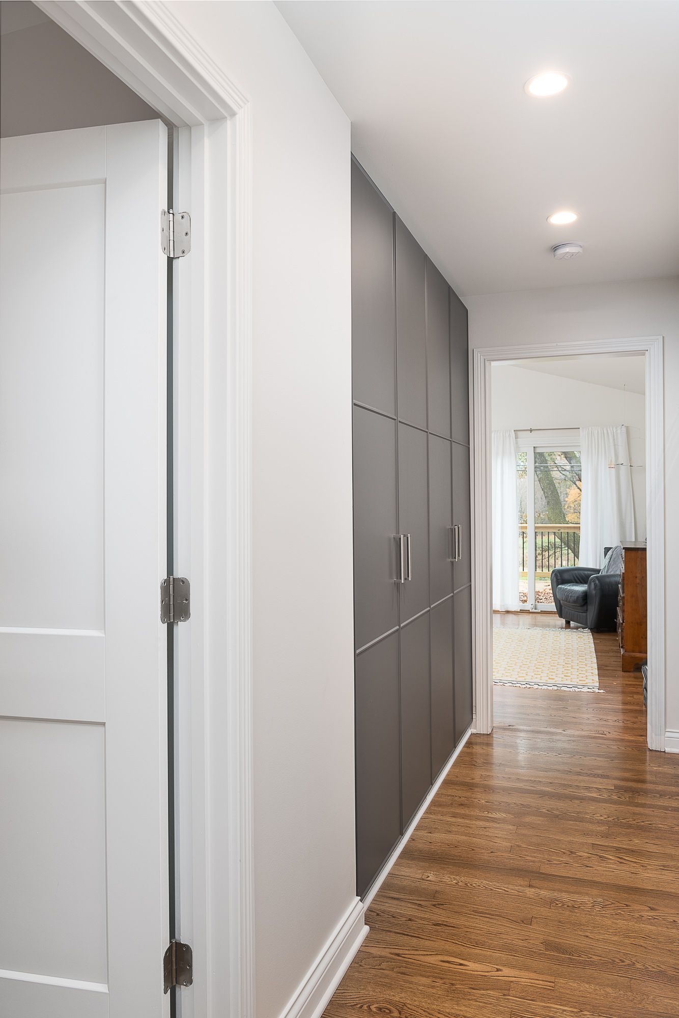 A hallway with a lot of cabinets and a door leading to a living room.