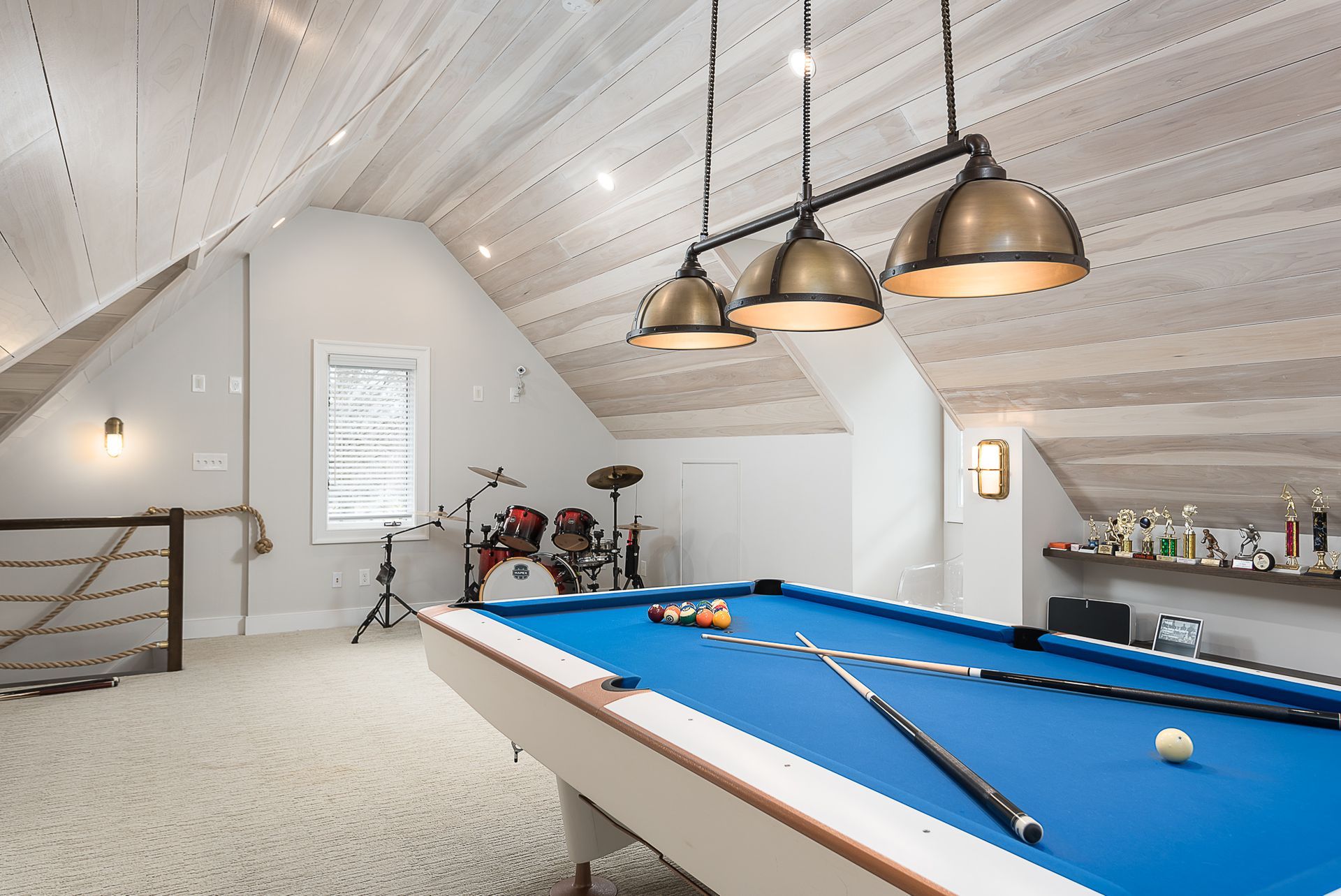 There is a pool table in the attic with a drum set in the background.