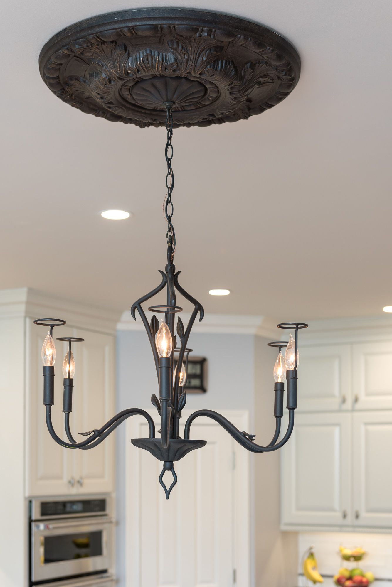 A black chandelier is hanging from the ceiling in a kitchen.