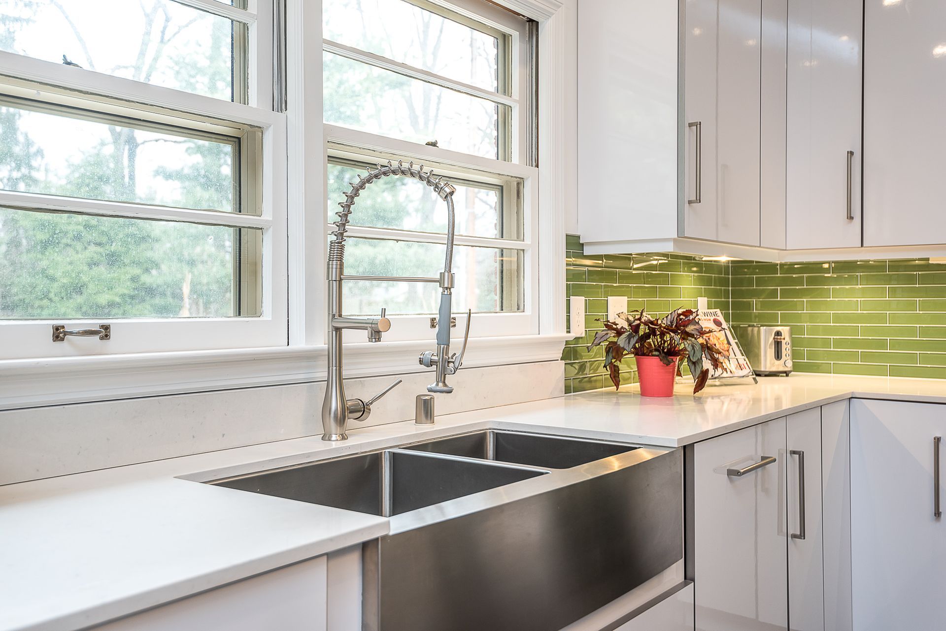 A kitchen with two sinks , white cabinets and green tiles.