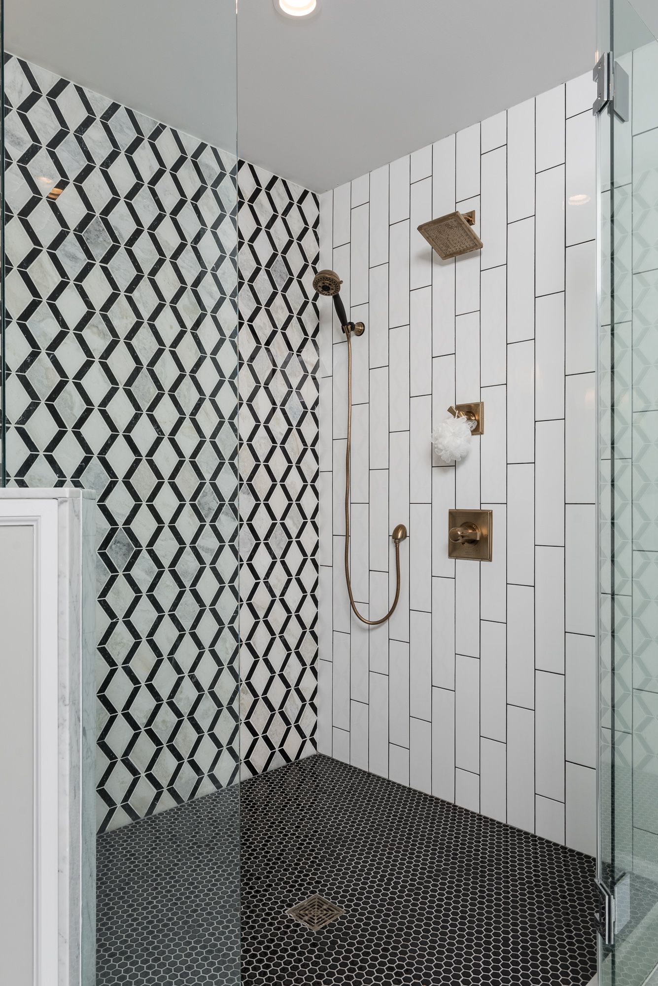 A walk in shower with black and white tiles and a glass door.