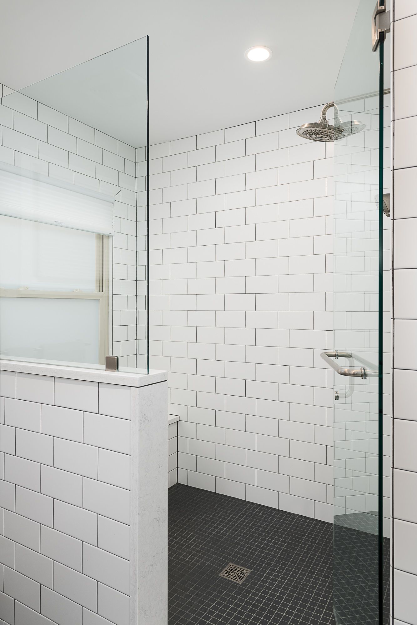 A bathroom with white tiles and a walk in shower with a glass door.