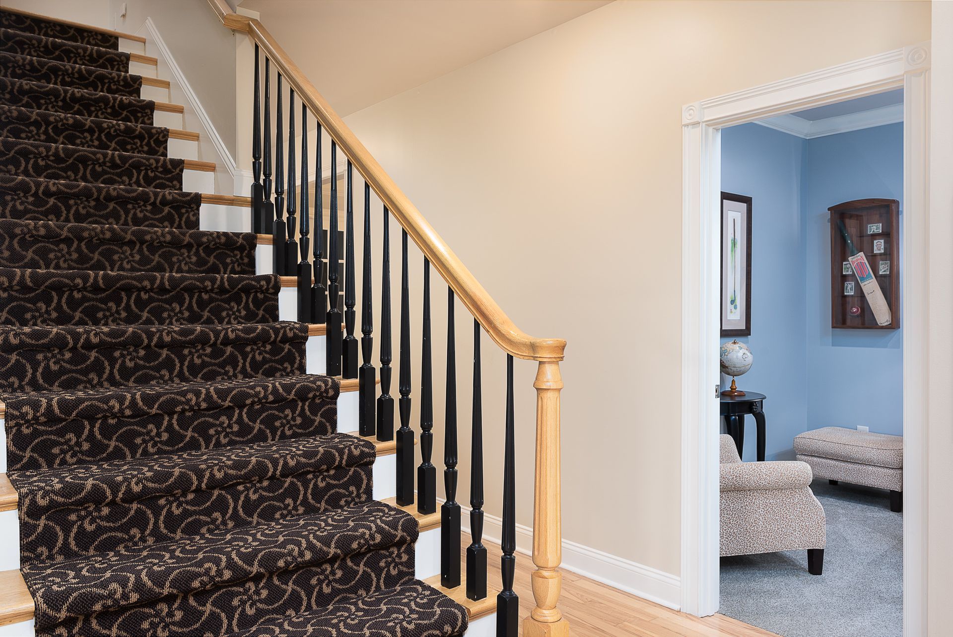 A staircase with a black carpet and a wooden railing leading up to a living room.