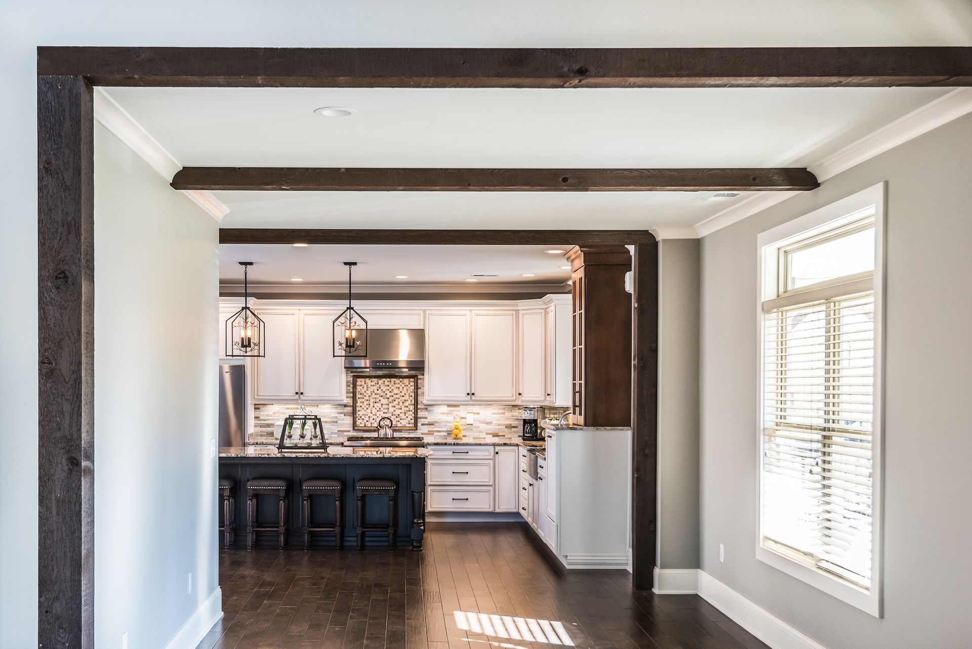 A kitchen with white cabinets , stainless steel appliances , and wooden beams.