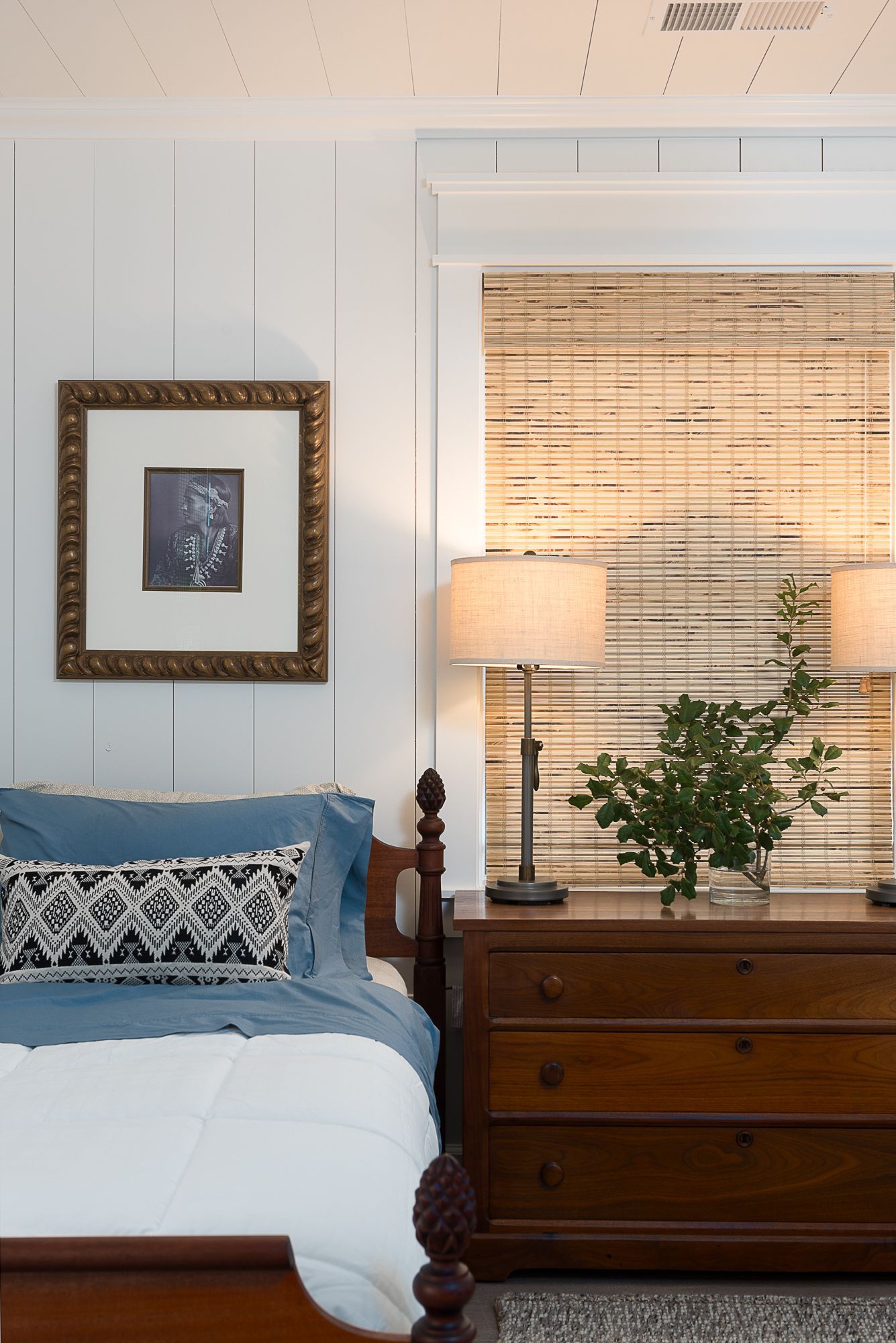 A bedroom with a bed a dresser and a picture on the wall