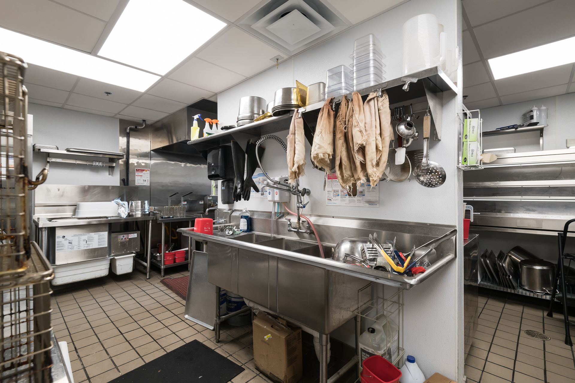 A kitchen with a stainless steel sink and utensils hanging on the wall.