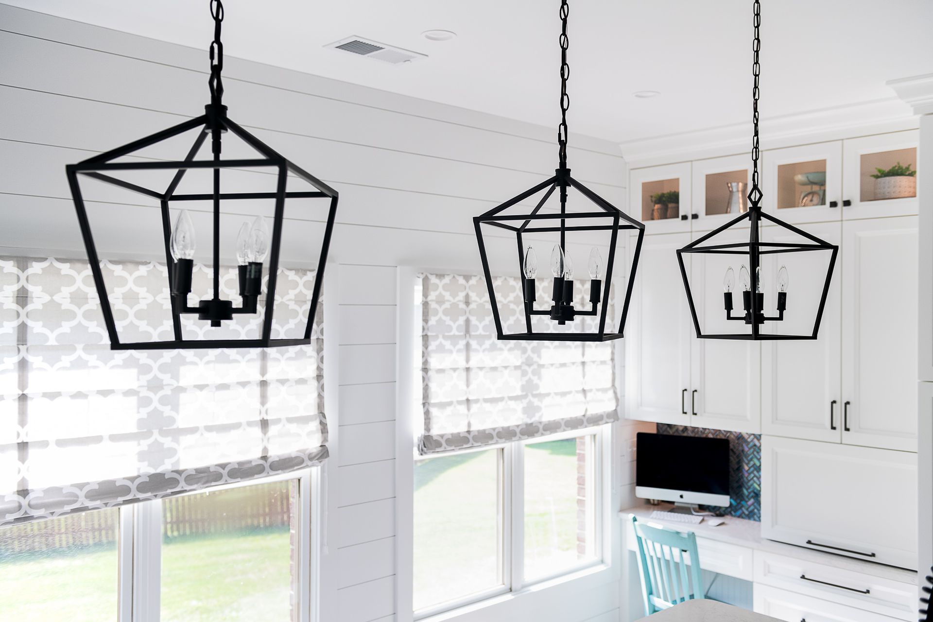 A kitchen with white cabinets and black lanterns hanging from the ceiling.