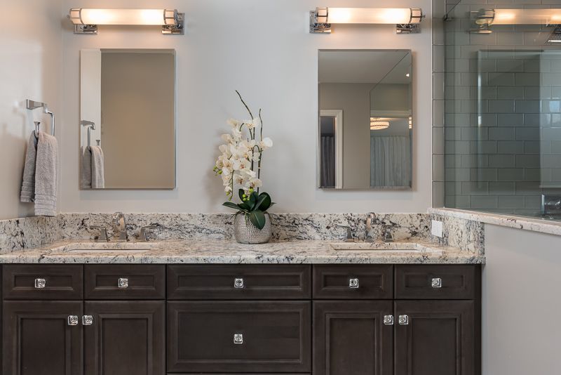 A bathroom with two sinks , two mirrors and a vase of flowers.