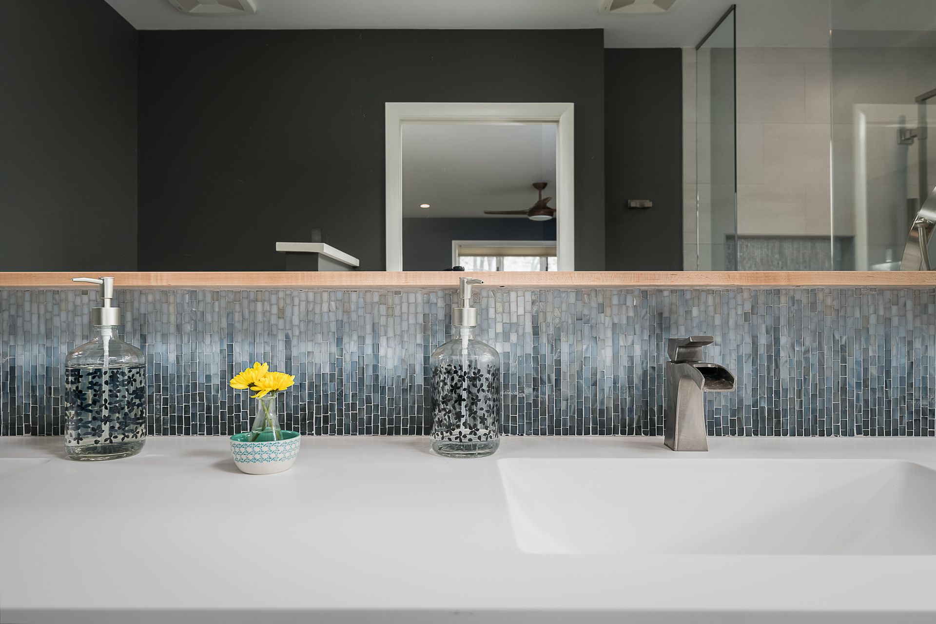 A bathroom with a sink , mirror and soap dispensers.