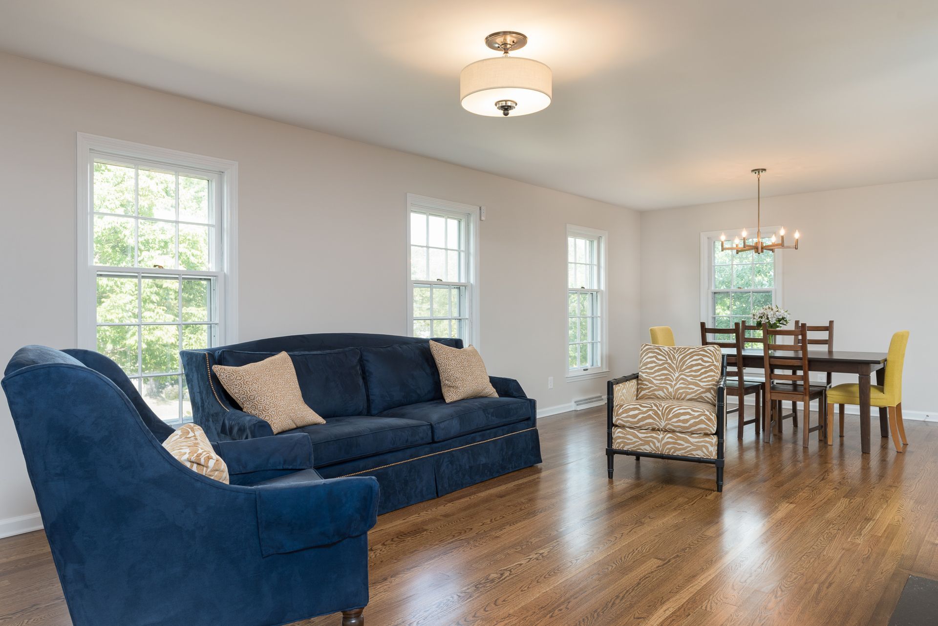 A living room with a blue couch , two chairs , a table and a chandelier.