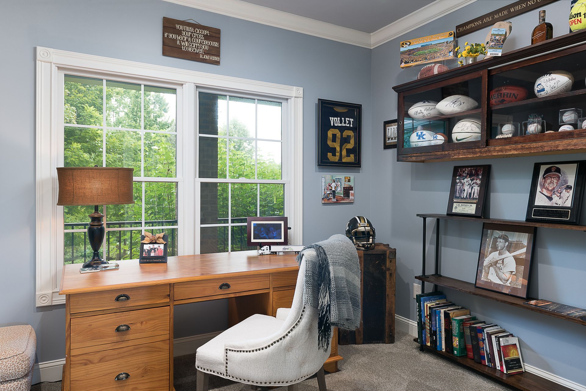 A home office with a desk , chair , lamp and shelves filled with footballs.