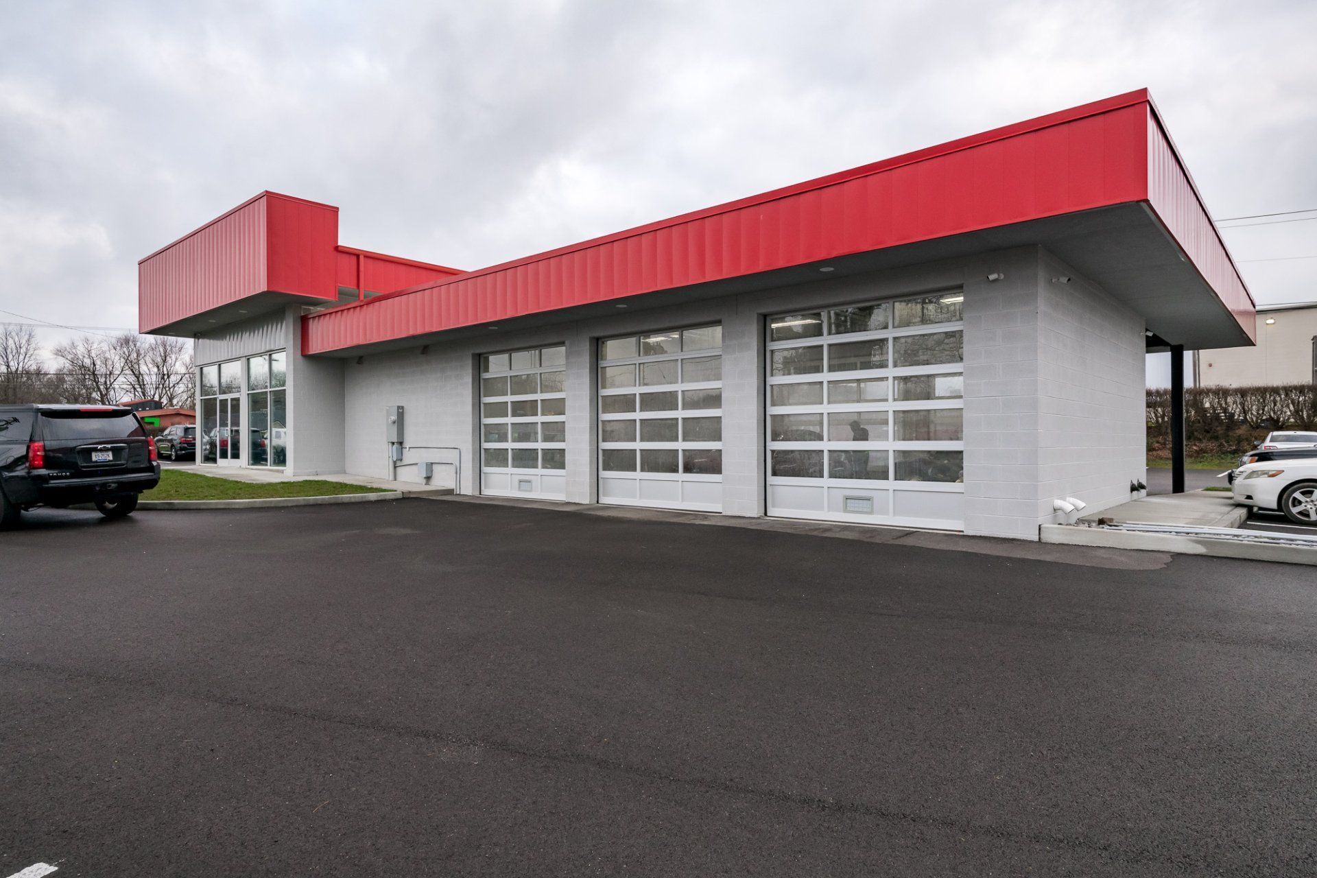 A car is parked in front of a white building with a red roof.