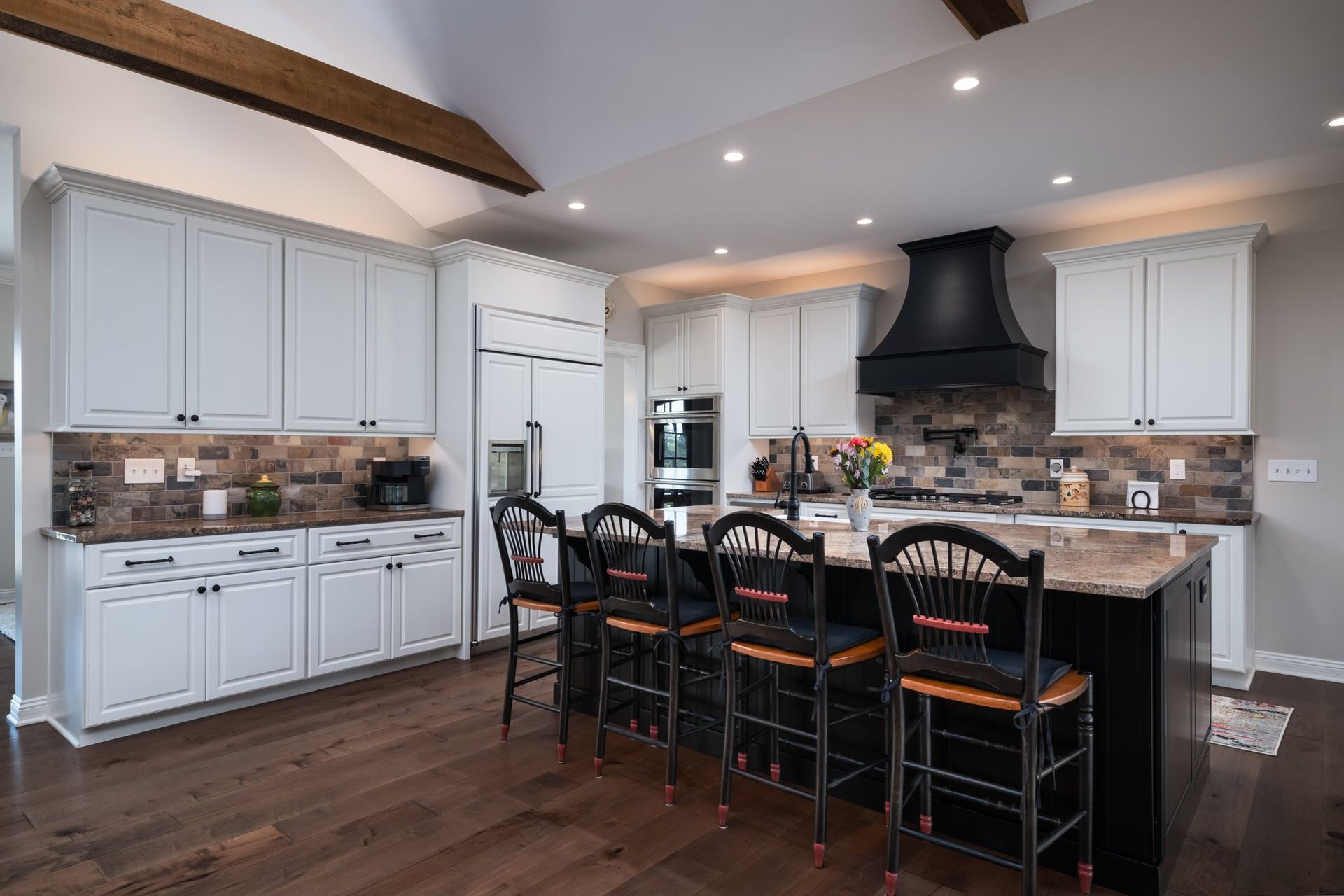 A kitchen with white cabinets , a large island , and stools.