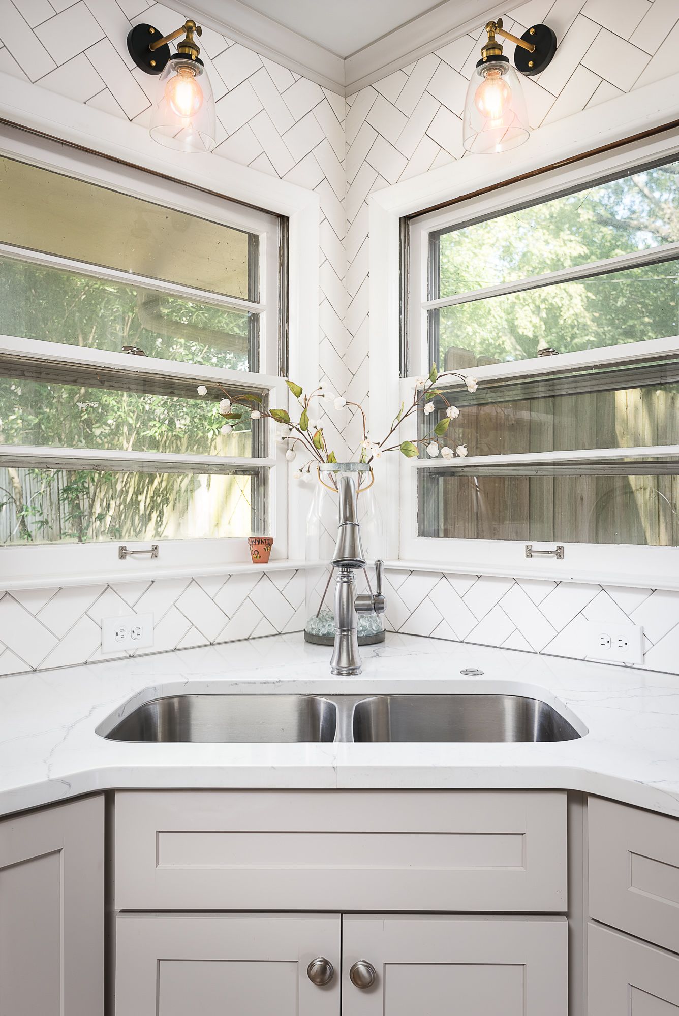 A kitchen with a sink , cabinets , and two windows.