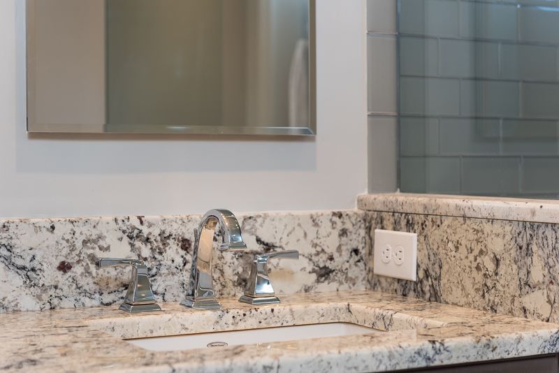 A bathroom sink with a granite counter top and a mirror.