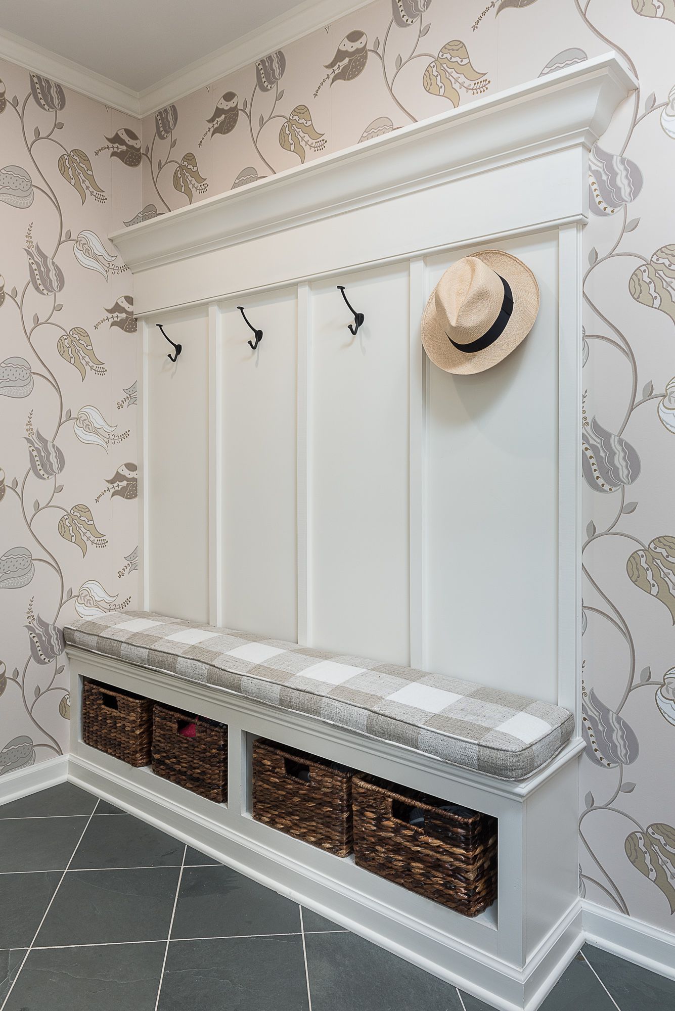 A hallway with a bench and baskets and a hat hanging on the wall.