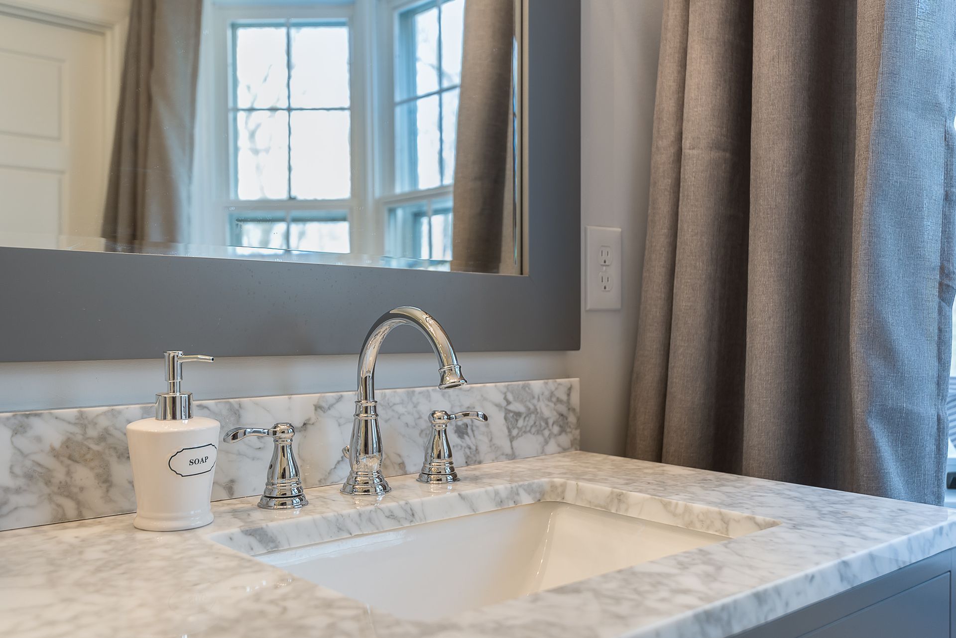 A bathroom with a sink , mirror and soap dispenser.