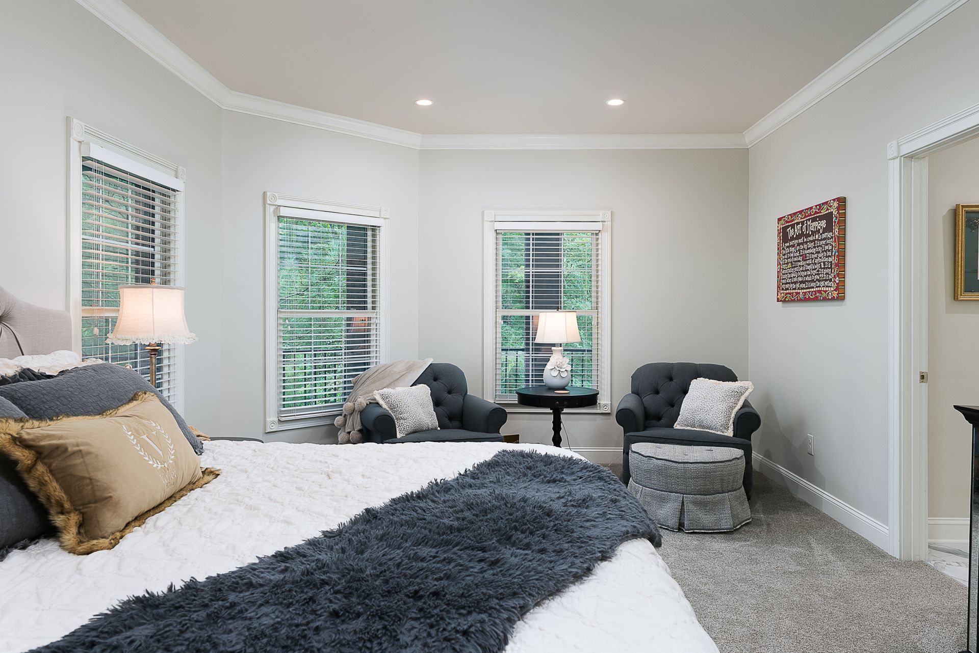 A bedroom with a large bed , two chairs , a table and two windows.