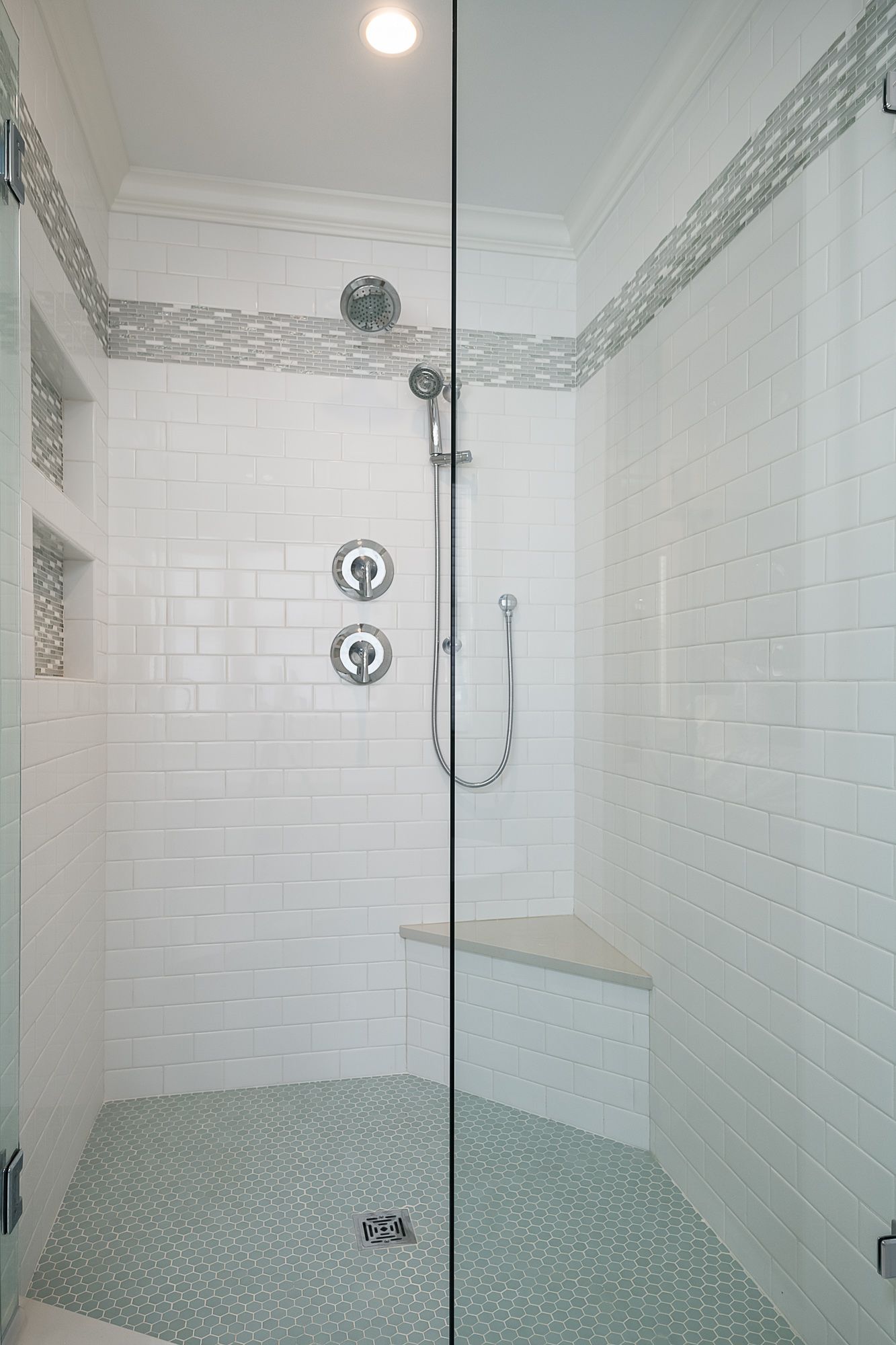 A walk in shower with a glass door and a bench.